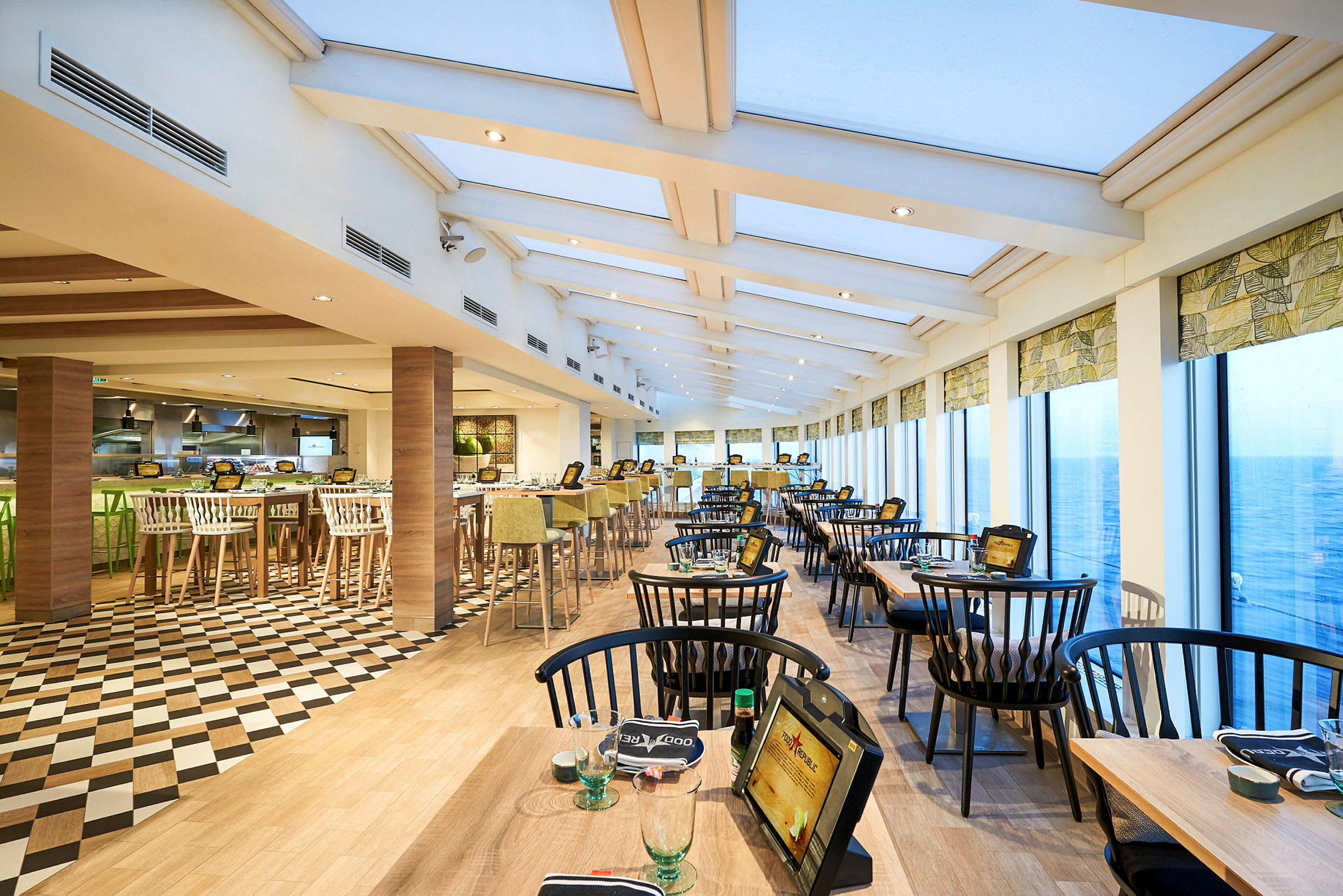 Udsigt over en restaurant med store vinduer og siddepladser arrangeret ved borde. (AI-genereret tekst)