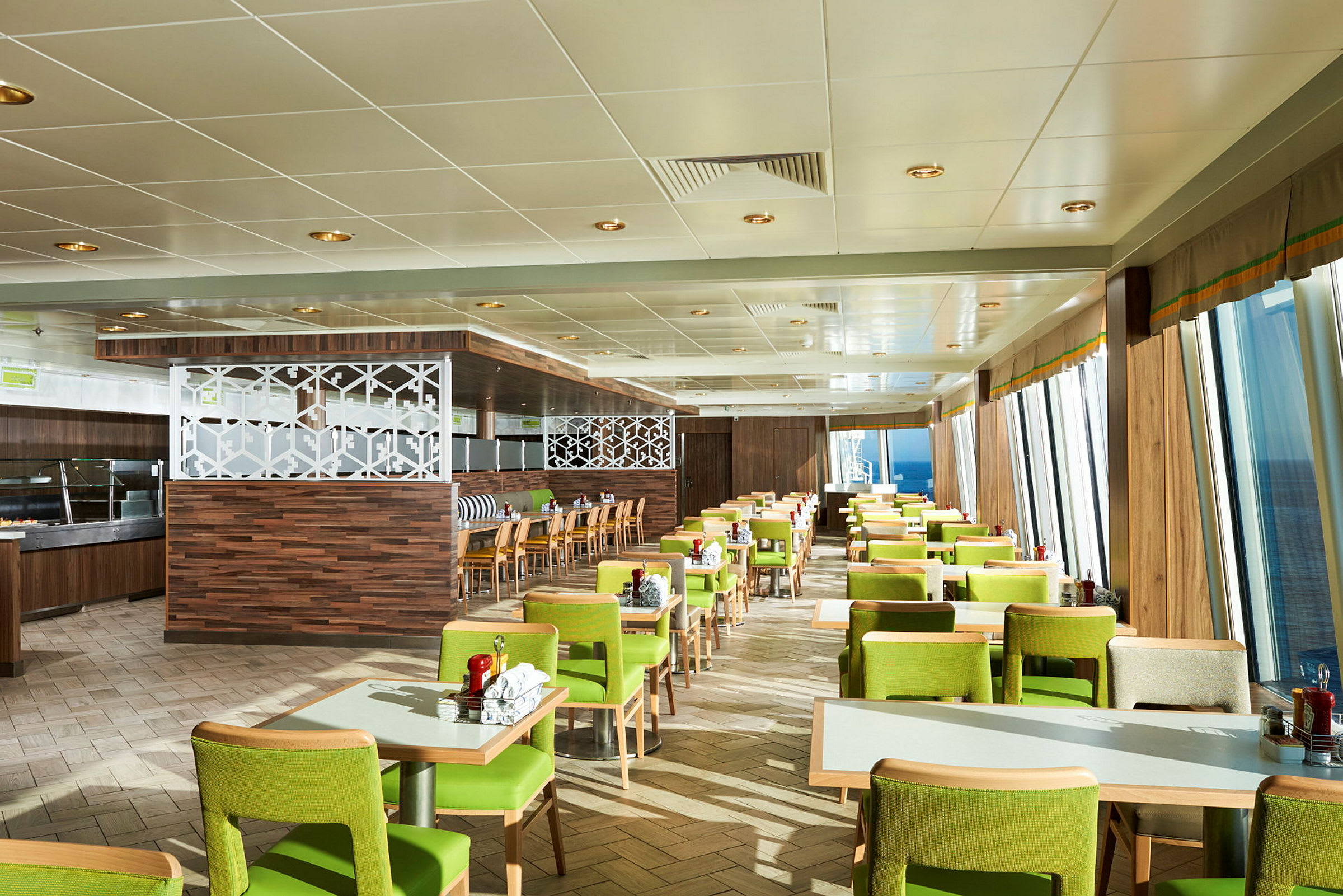 En restaurant med grønklædte stole og borde placeret i rækker, med vinduer der viser havet udenfor. (AI-genereret tekst)