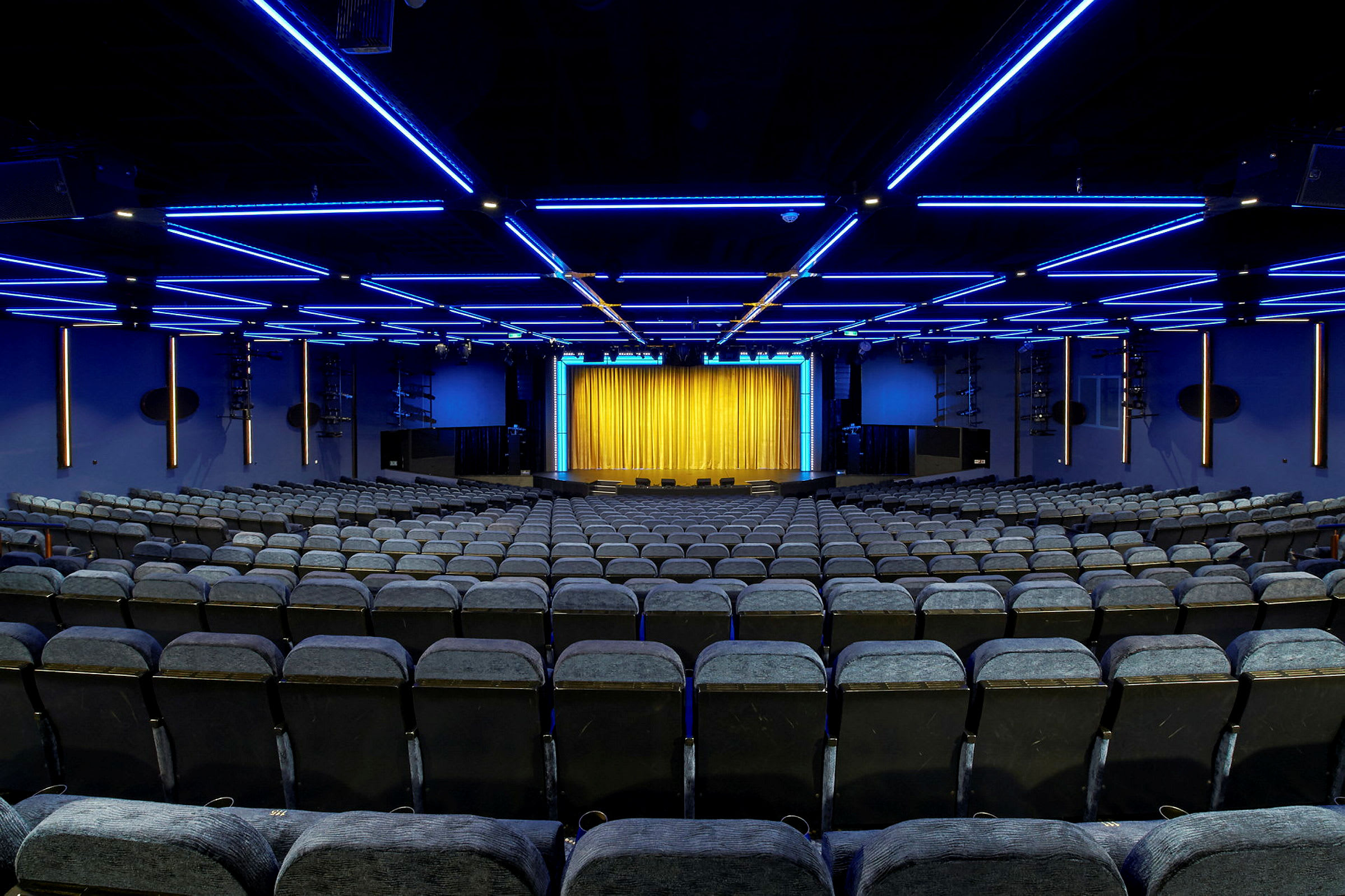En teatersal med stole i rækker og en scene med et gult gardin. (AI-genereret tekst)