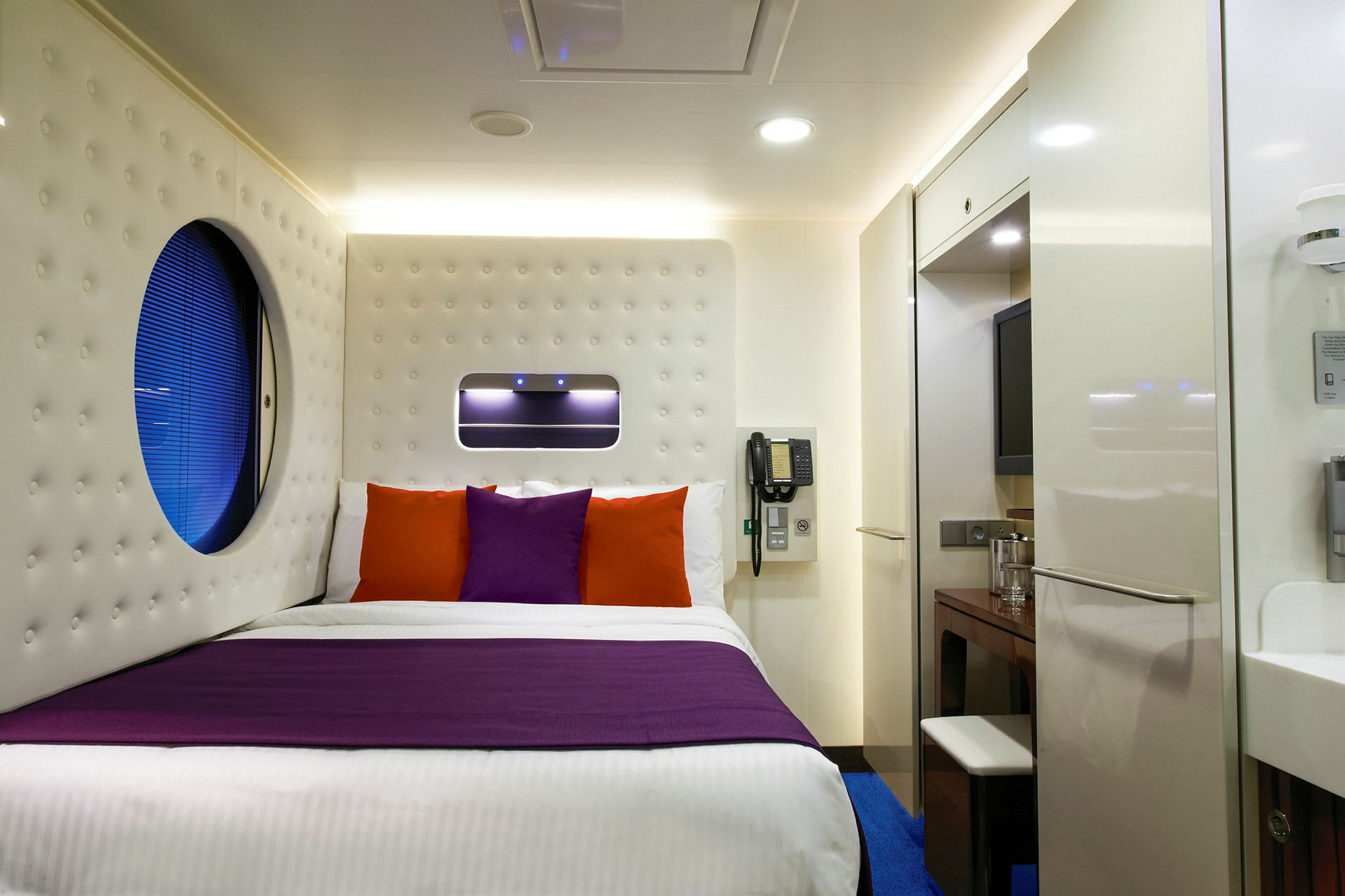 Et moderne hotelværelse med en seng med lilla og orange puder. (AI-genereret tekst)