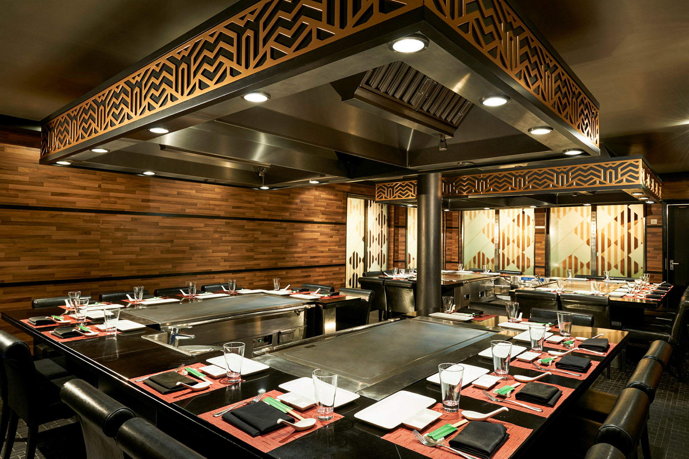 Et teppanyaki-restaurantbord med elegant opdækning, omgivet af træpaneler og belysning. (AI-genereret tekst)