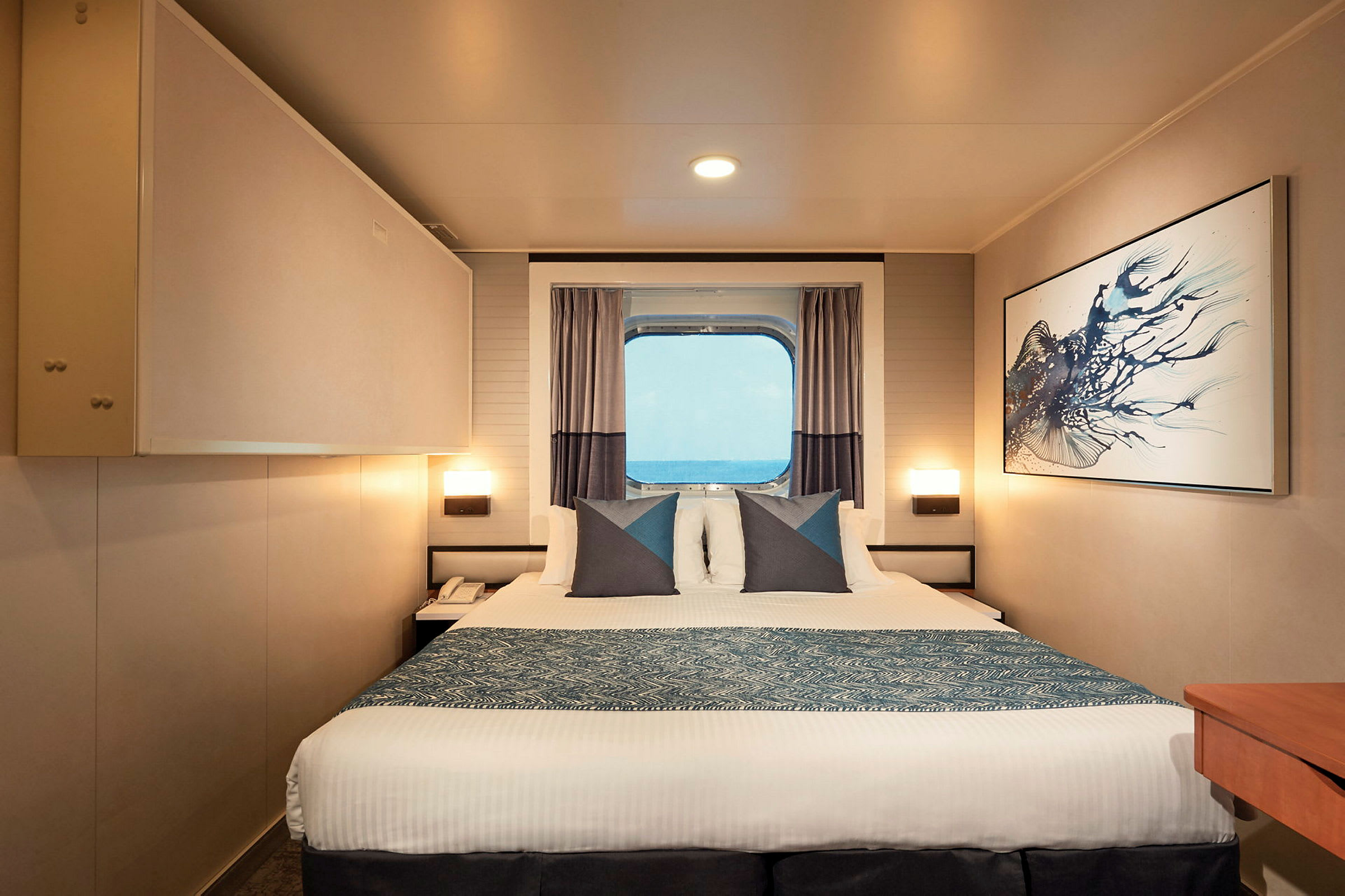 Et hotelværelse med en seng, kunst på væggen og et vindue med udsigt over havet. (AI-genereret tekst)