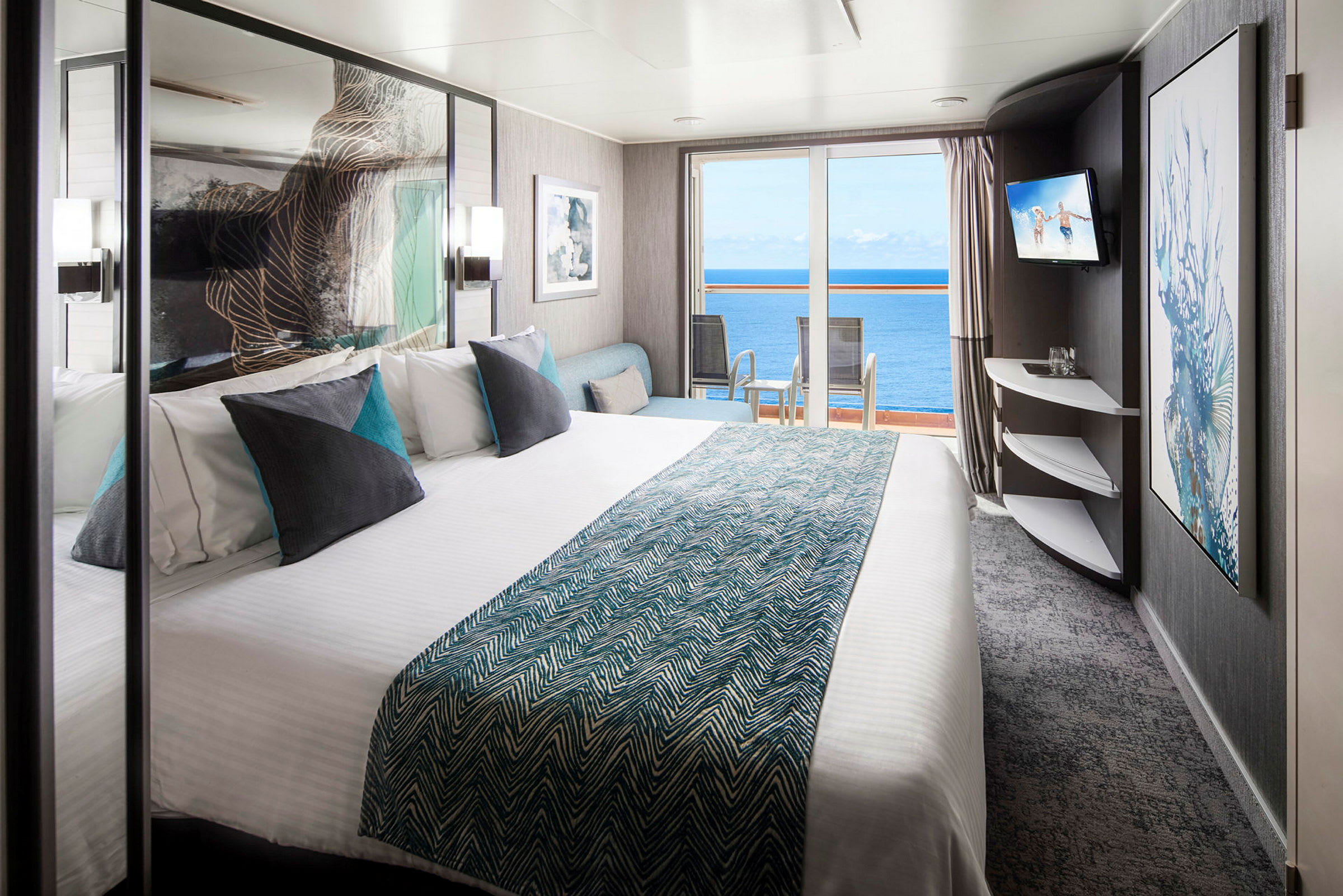 Hotelværelse med dobbeltseng, puder og udsigt til havet gennem glasdøre. (AI-genereret tekst)
