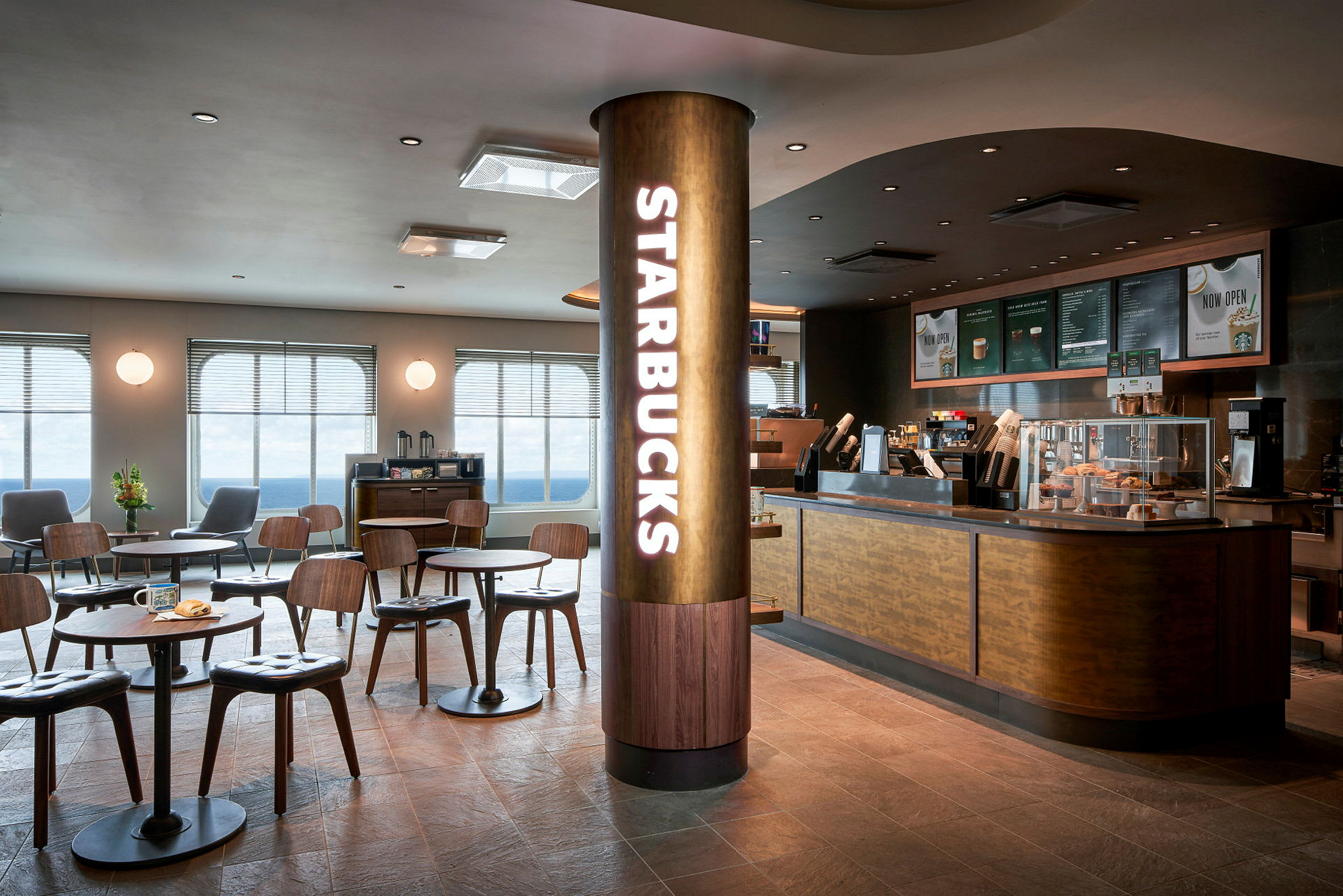 En moderne café med Starbucks-logo på en søjle og siddepladser med borde foran en serveringsdisk. (AI-genereret tekst)