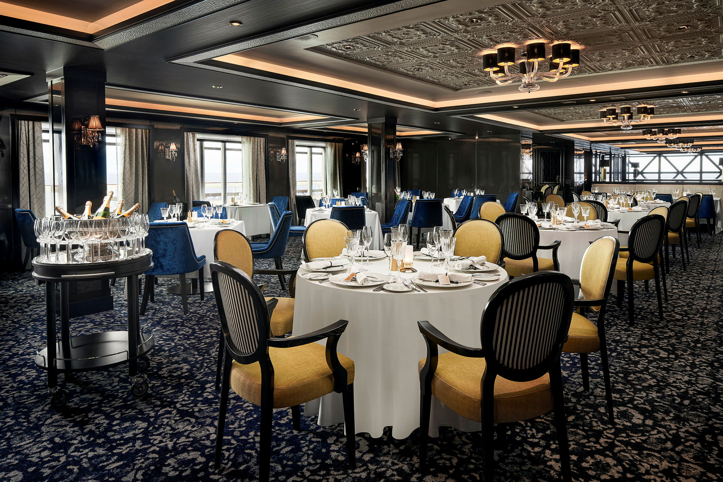 Billede af en elegant restaurant med dækkede borde, komfortable stole og en serveringsvogn med glas og flasker. (AI-genereret tekst)