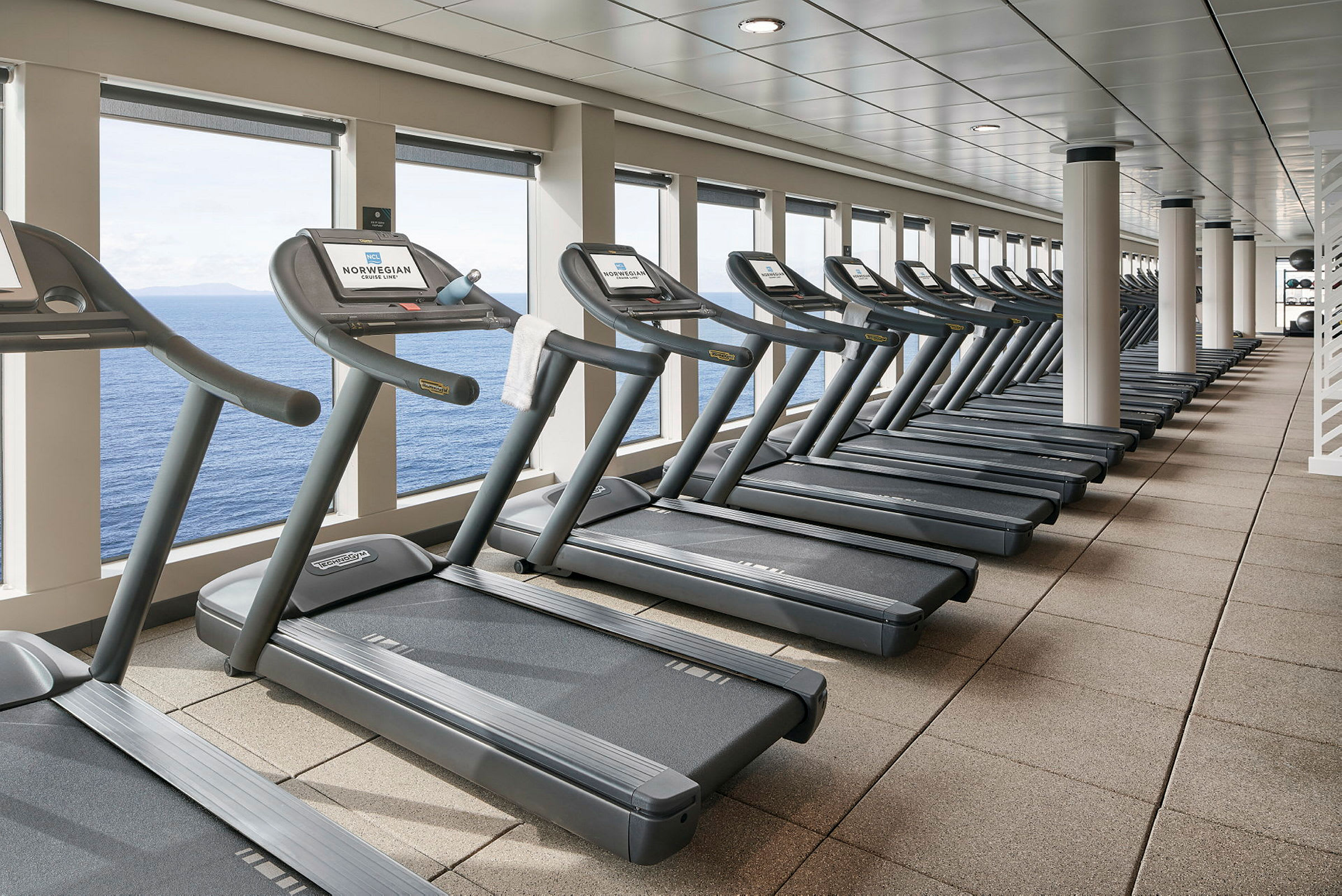 En række løbebånd i et motionscenter med udsigt over havet. (AI-genereret tekst)