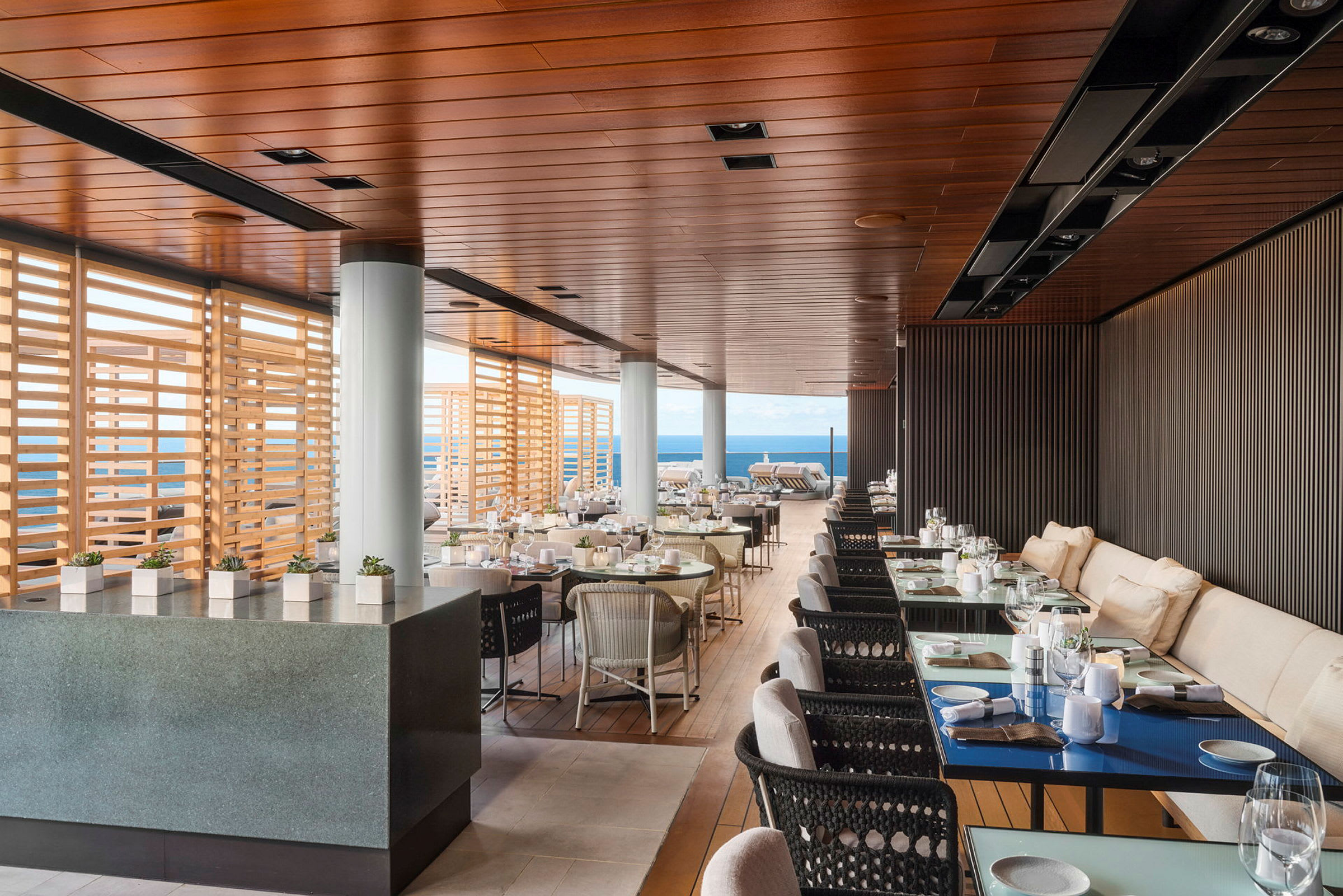En elegant restaurant med havudsigt, indendørs og udendørs områder, med trædetaljer og moderne indretning. (AI-genereret tekst)