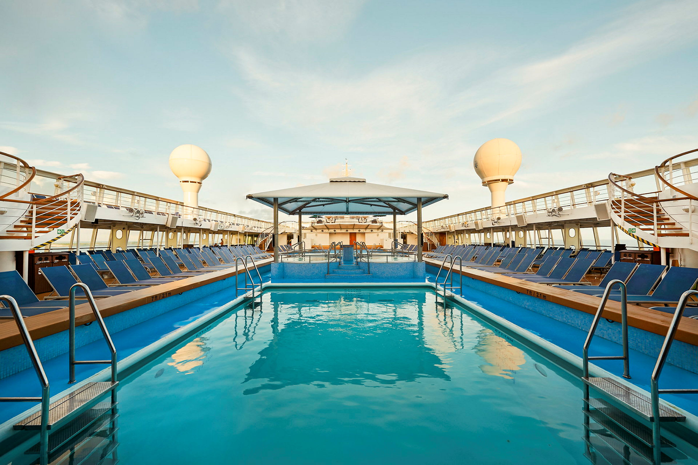 Billede af en udendørs swimmingpool på et krydstogtskib med solsenge rundt om.  (AI-genereret tekst)