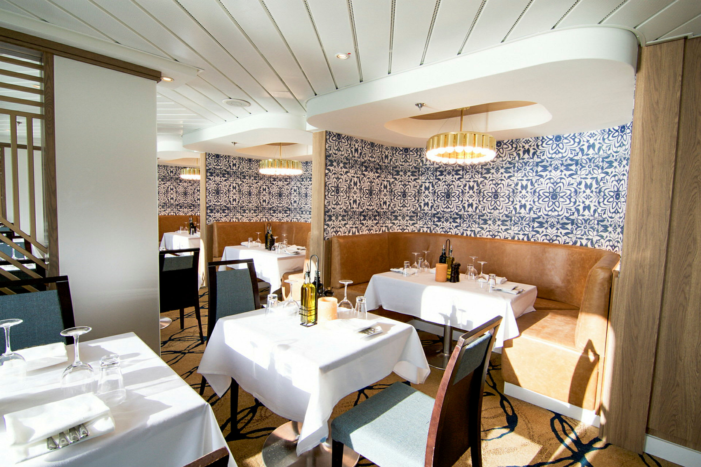 En elegant restaurant med hvide duge, blåmønstrede tapeter og moderne lysekroner. (AI-genereret tekst)