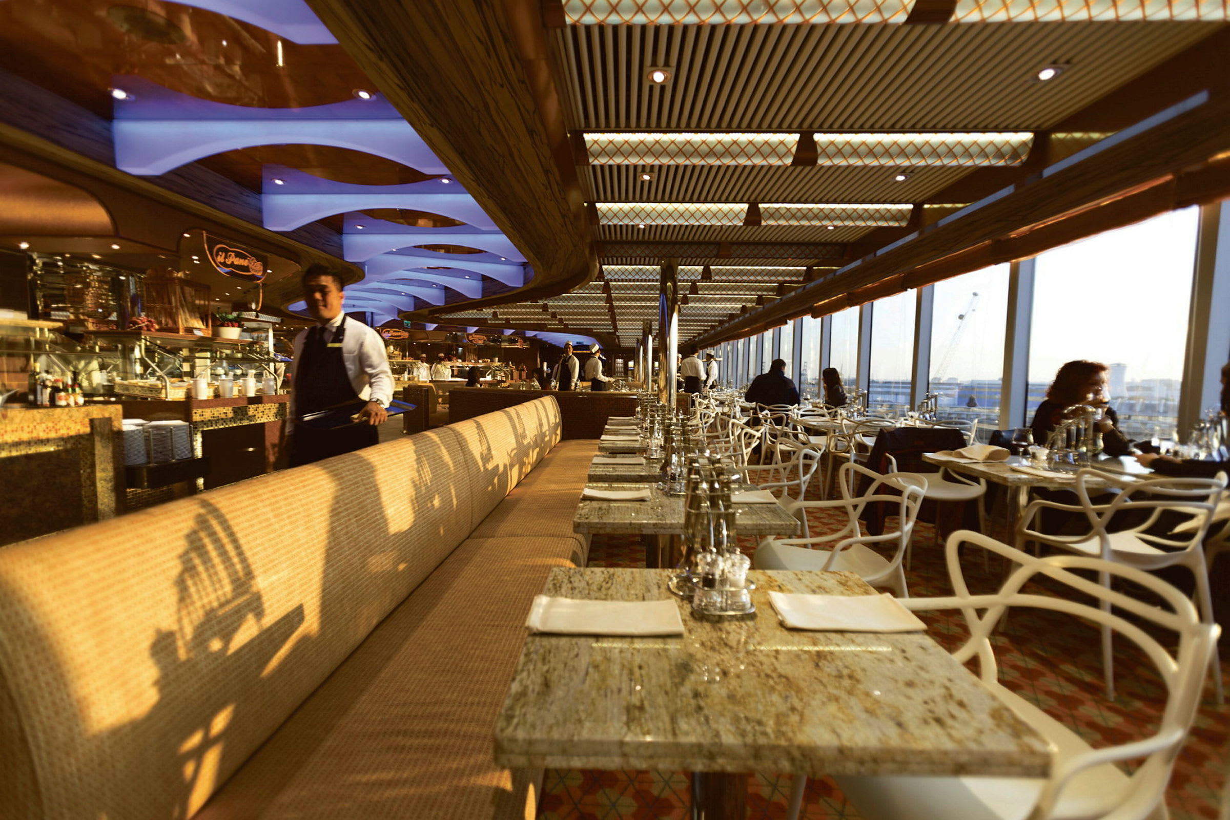 Restaurantmiljø med borde og bænke, store vinduer og udsigt over byen. (AI-genereret tekst)