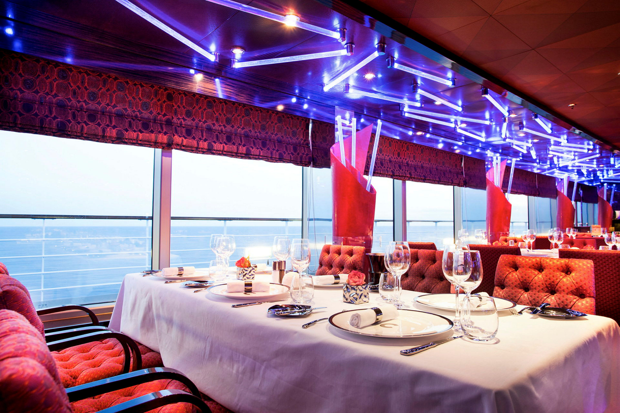 Elegant restaurantinteriør med dækket bord og havudsigt gennem panoramavinduer. (AI-genereret tekst)