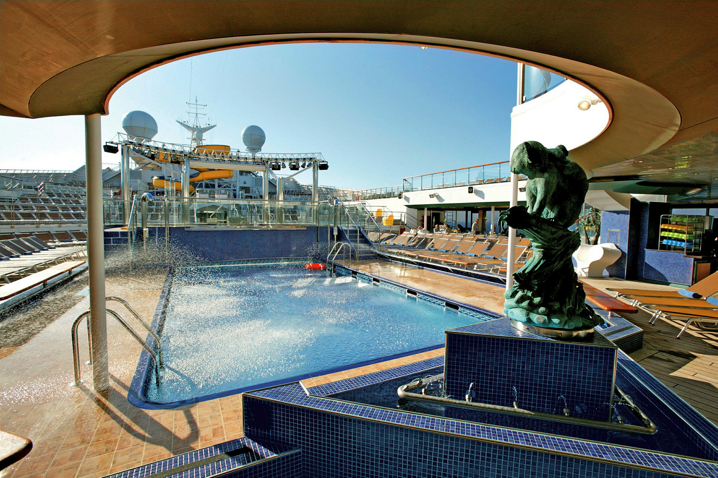 En blå pool omgivet af liggestole på dækket af et krydstogtskib, med en statue i forgrunden. (AI-genereret tekst)