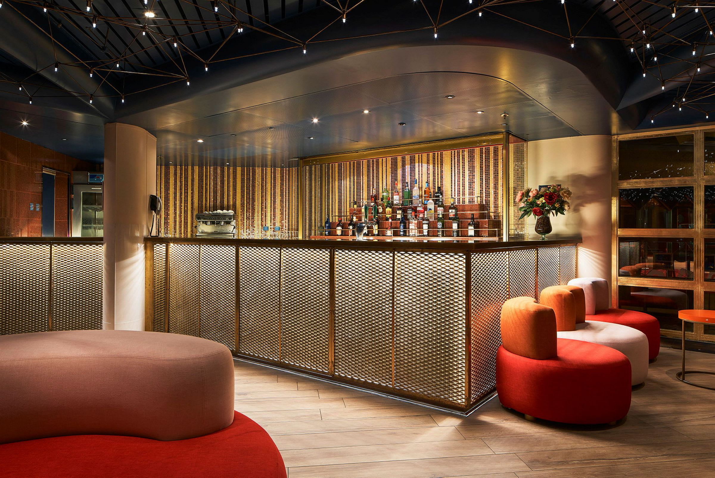 En elegant bar med gulddetaljeret front, siddepladser i forskellige farver og varm belysning. (AI-genereret tekst)