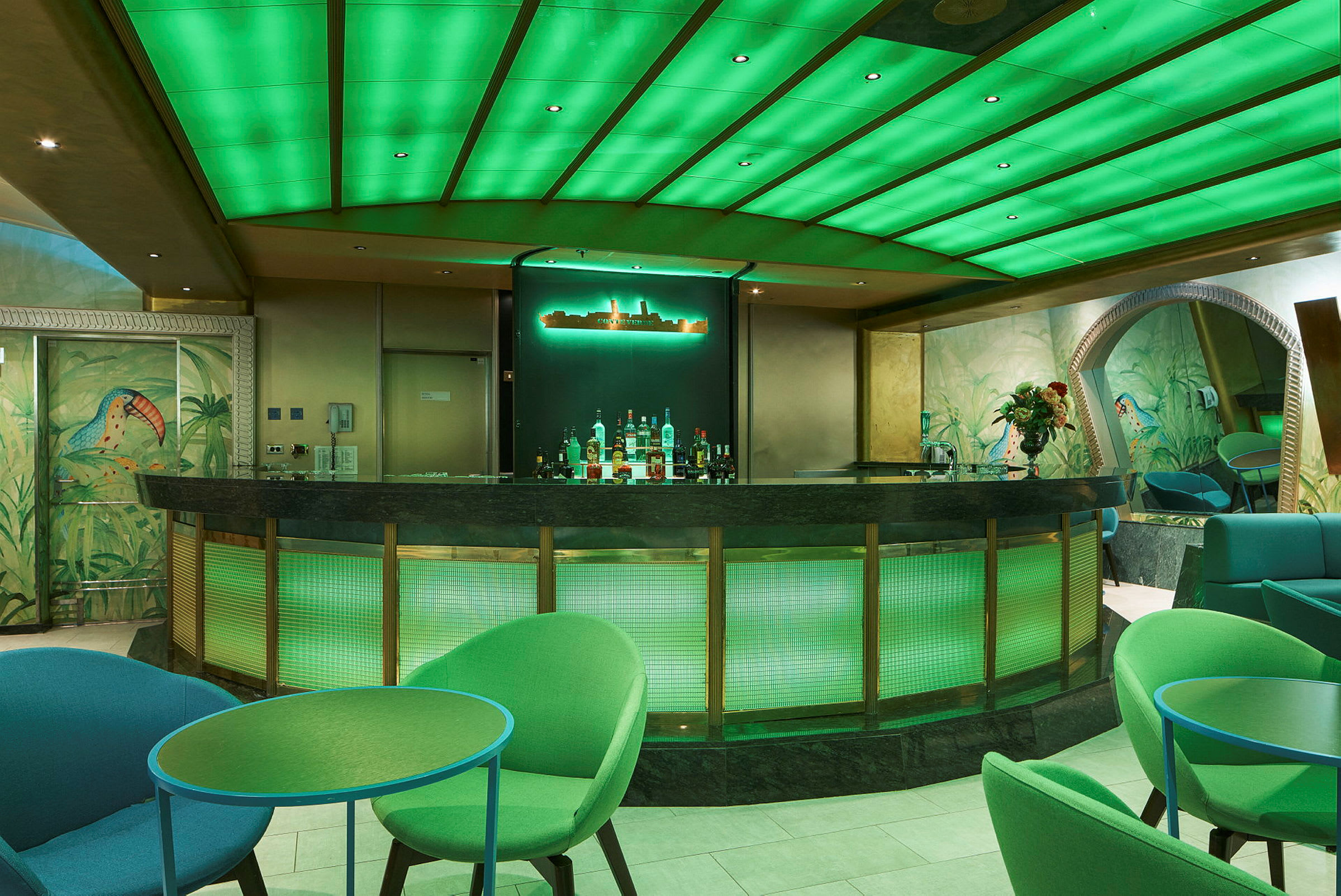 En bar med grønt oplyst loft og interiør. Farvede stole og borde findes i miljøet. (AI-genereret tekst)