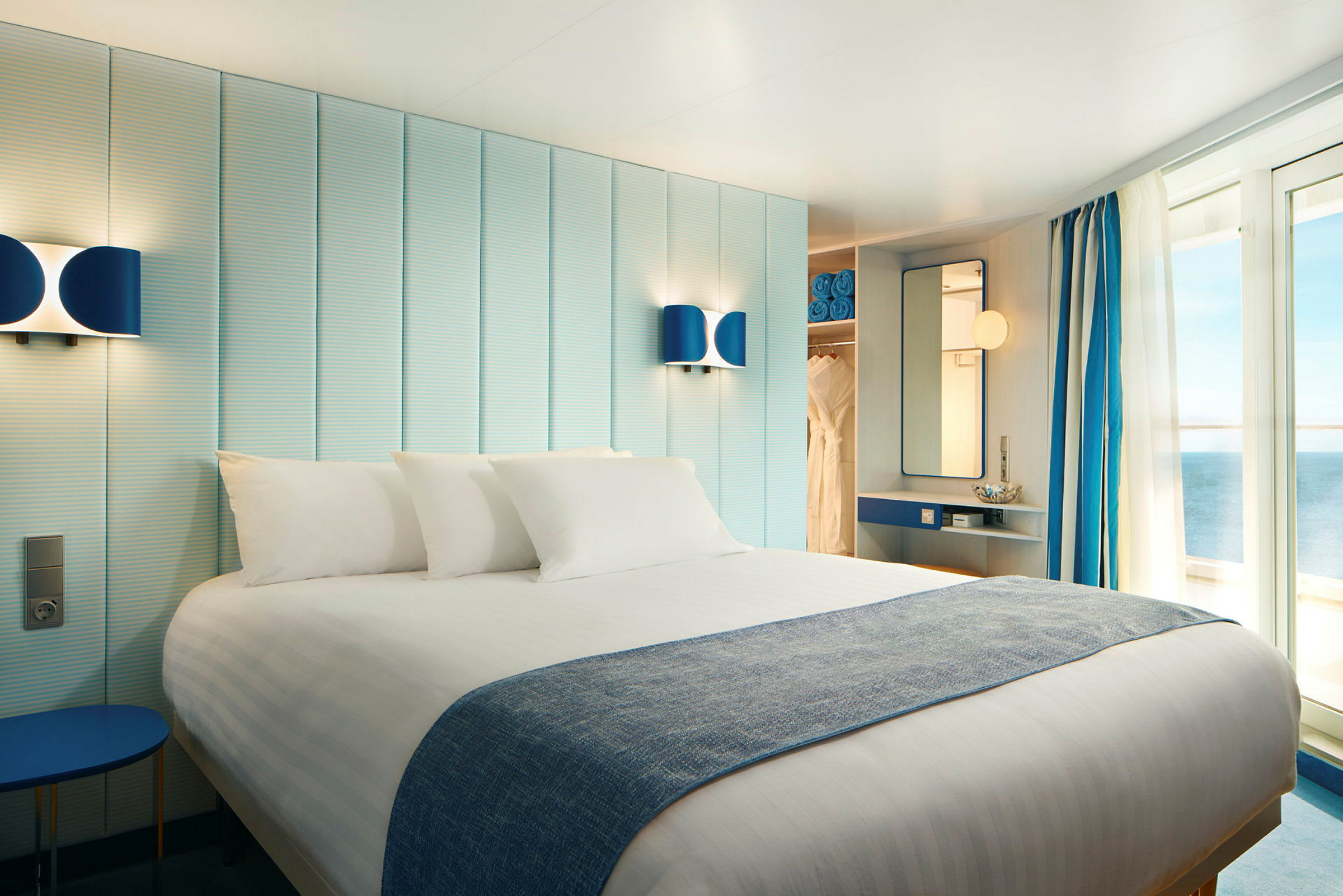 Et hotelværelse med en dobbeltseng, lys indretning og altandøre, der vender ud mod havet. (AI-genereret tekst)