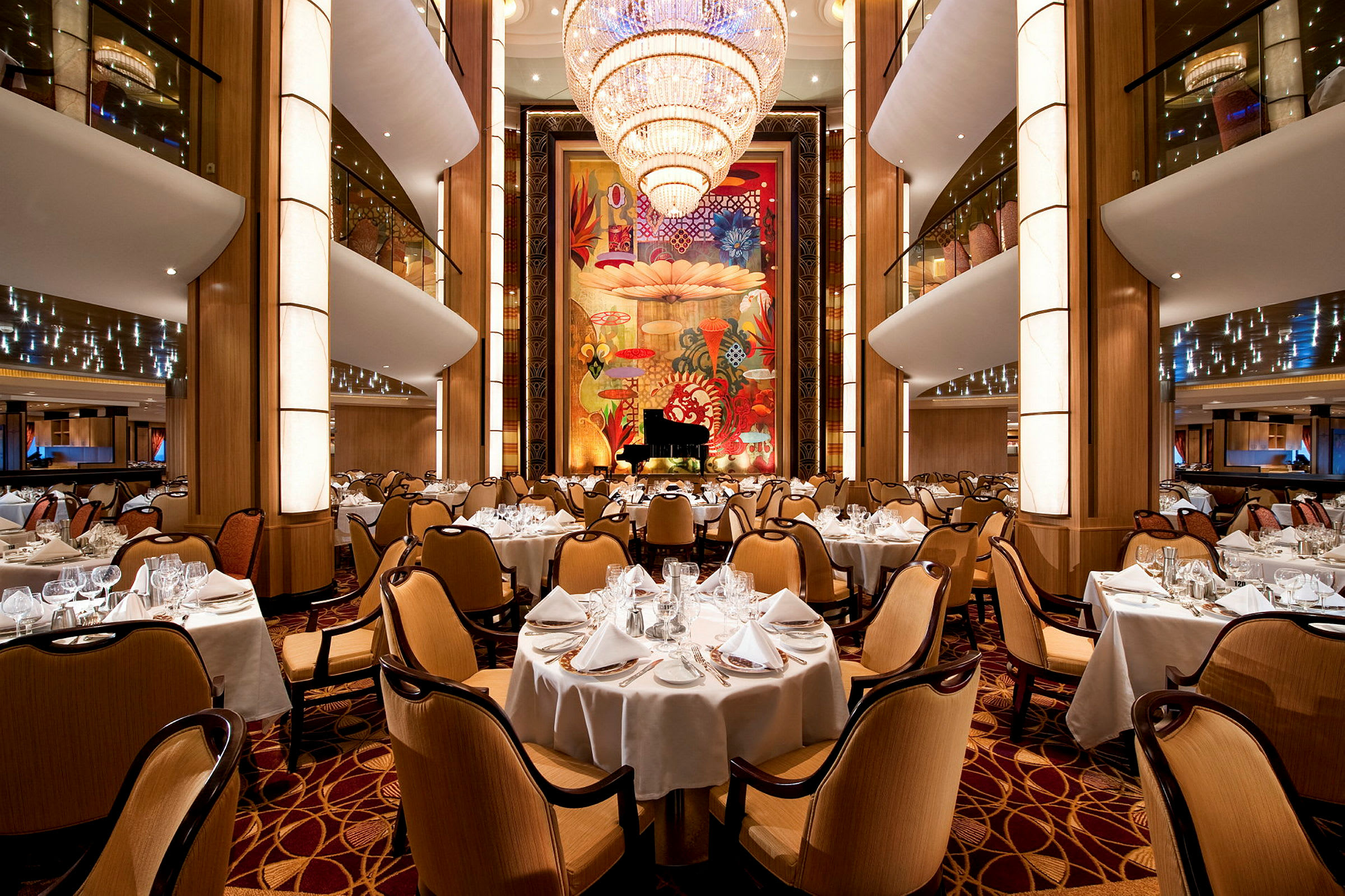 En rummelig restaurant med elegant indretning, runde borde og stole samt en stor lysekrone hængende fra loftet. (AI-genereret tekst)