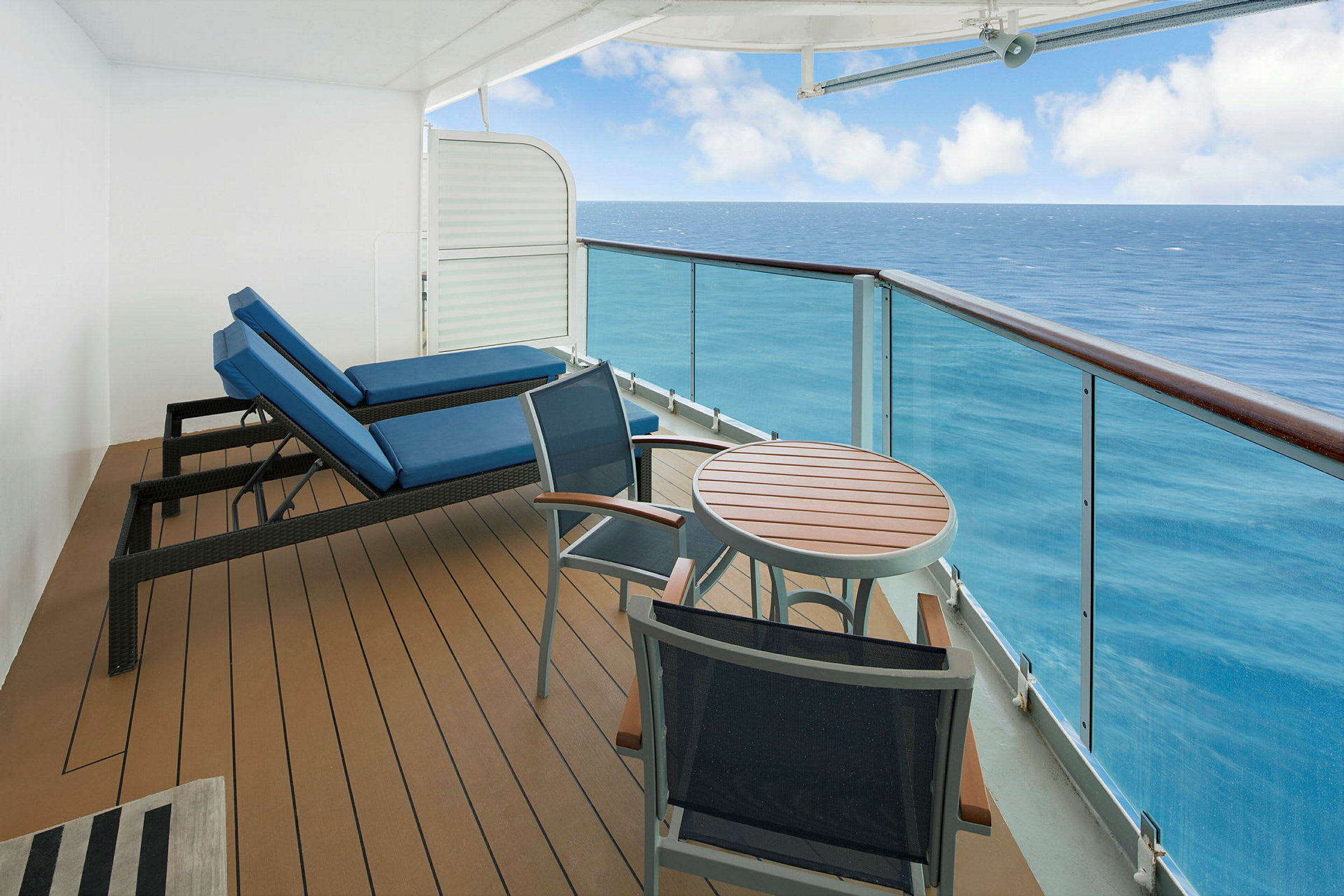 En balkon med to liggestole og et bord med stole mod havet. (AI-genereret tekst)