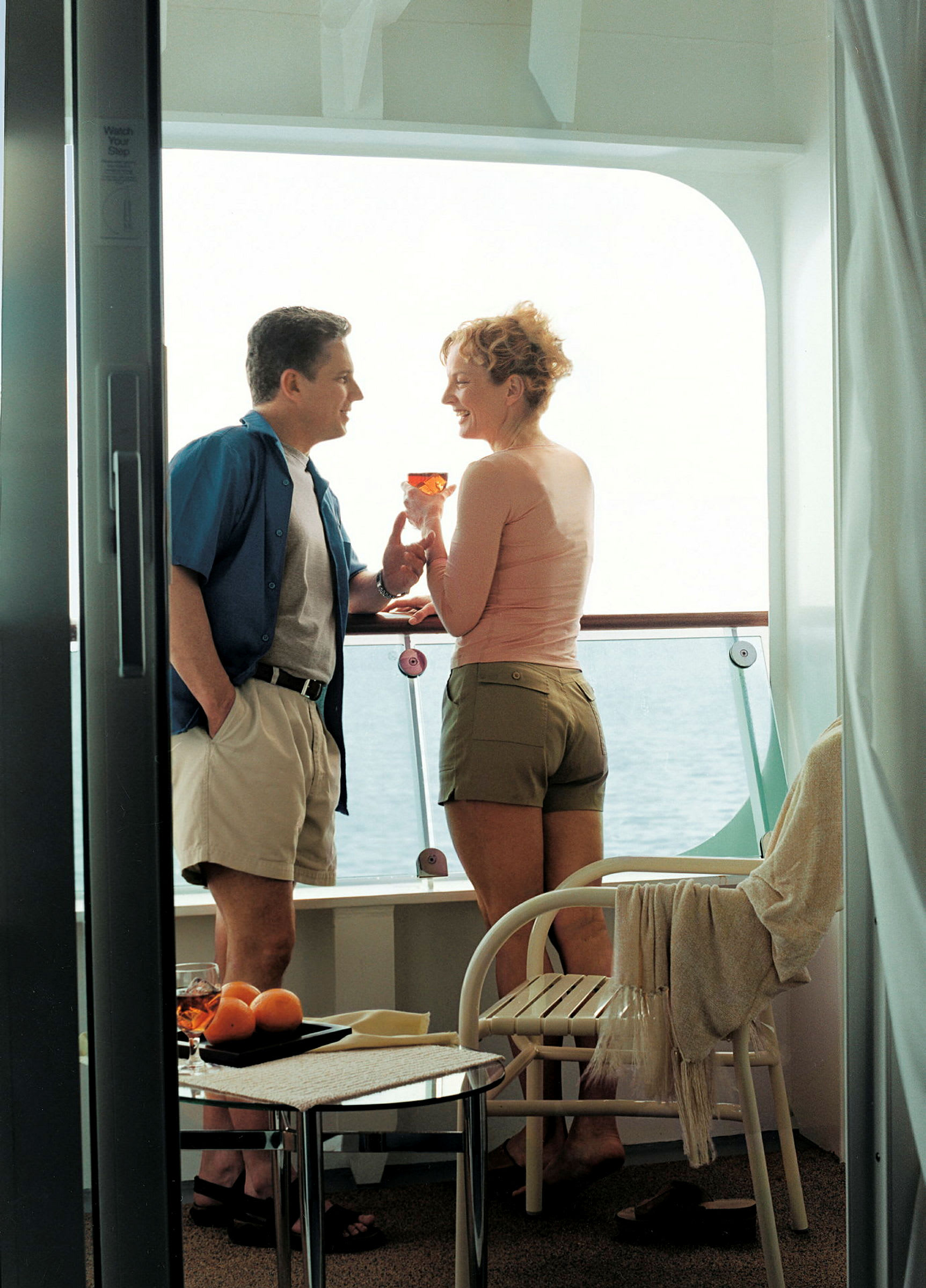 To personer står på en balkon med havudsigt og holder glas. (AI-genereret tekst)