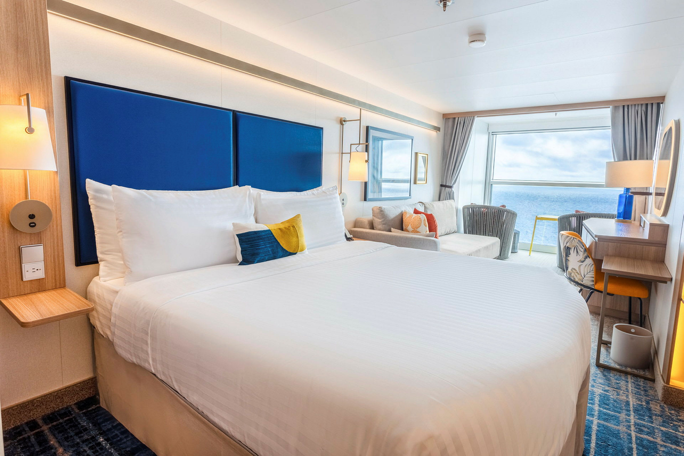 Et lyst hotelværelse med en stor seng, siddeområde og udsigt over havet. (AI-genereret tekst)