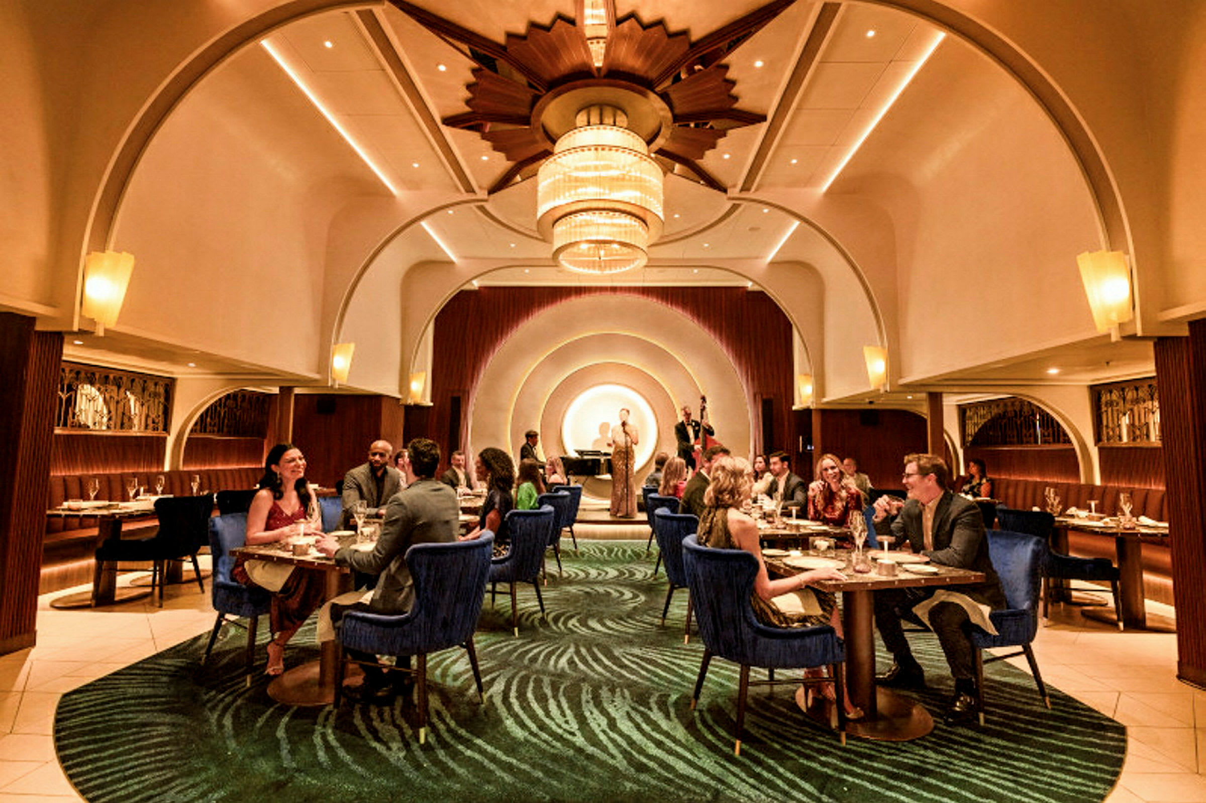En elegant restaurant med gæster, der sidder ved borde, og en scene i baggrunden med musikere. (AI-genereret tekst)