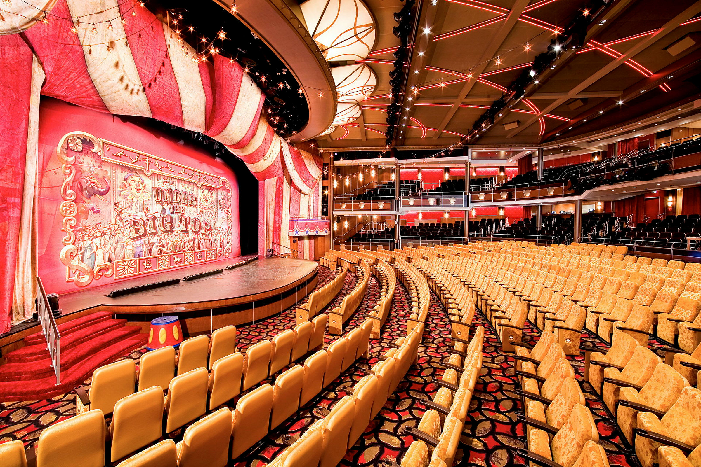 En teatersal med røde og gule dekorationer omkring scenen og publikumspladser. (AI-genereret tekst)