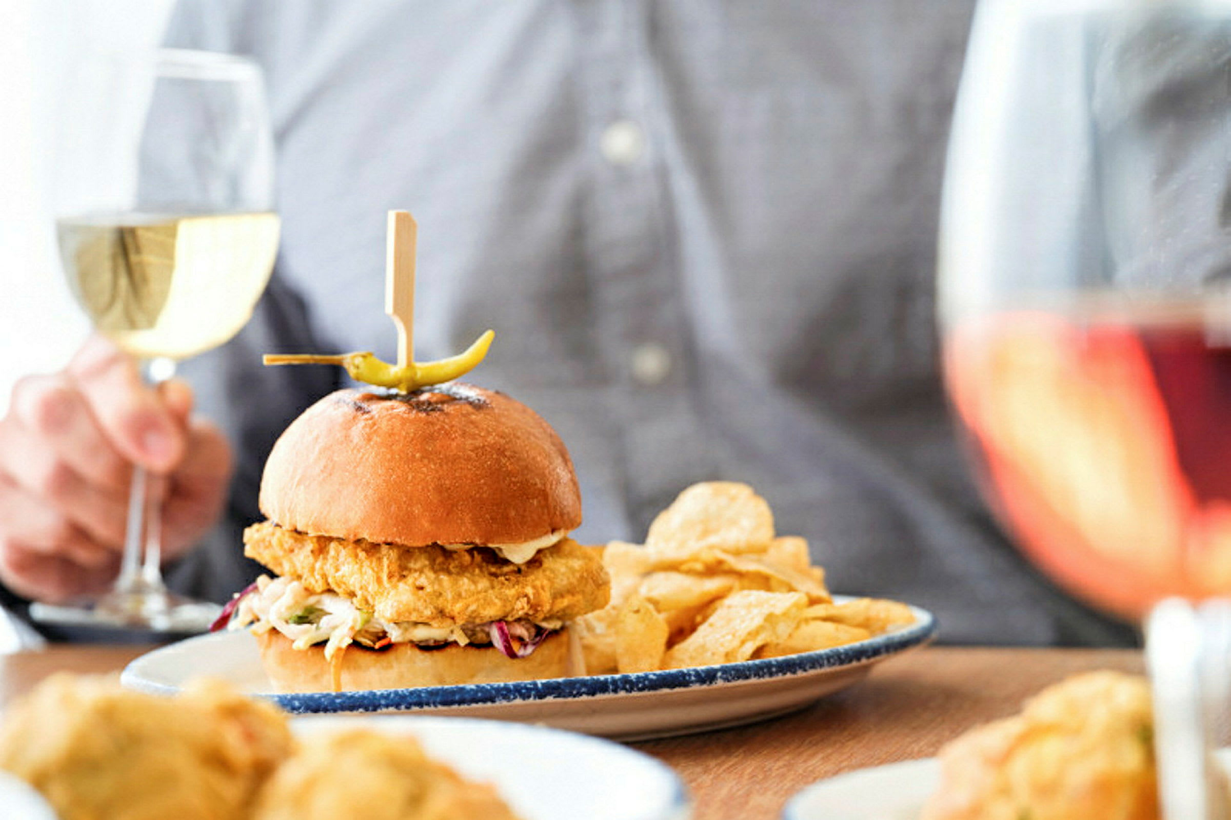 En tallerken med en burger, chips og et glas vin ses på billedet. (AI-genereret tekst)