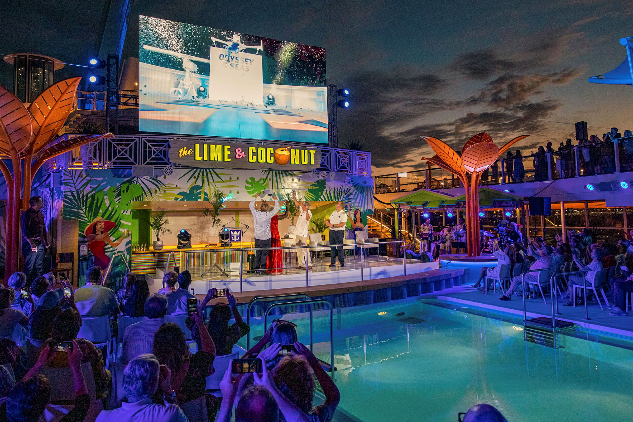En scene ved en pool med en stor skærm, dekoreret med tropiske motiver og teksten "The Lime & Coconut". (AI-genereret tekst)