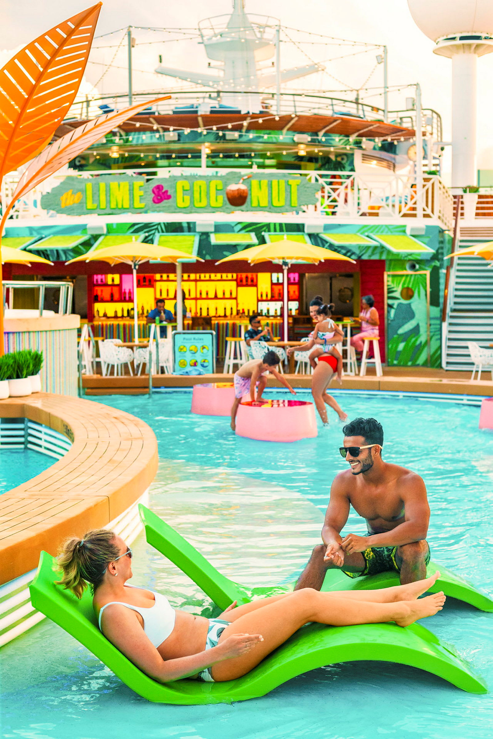 En pool omgivet af mennesker, der nyder solen og svømning, med en farverig bar i baggrunden. (AI-genereret tekst)