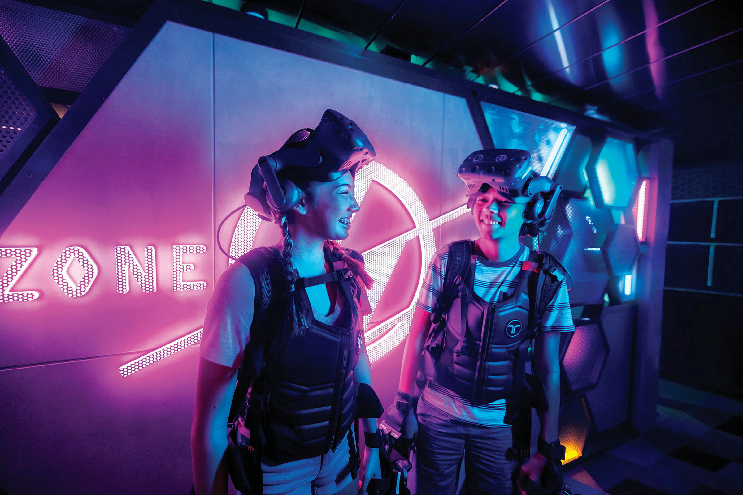 To personer i et futuristisk miljø med VR-udstyr og neonlys. (AI-genereret tekst)