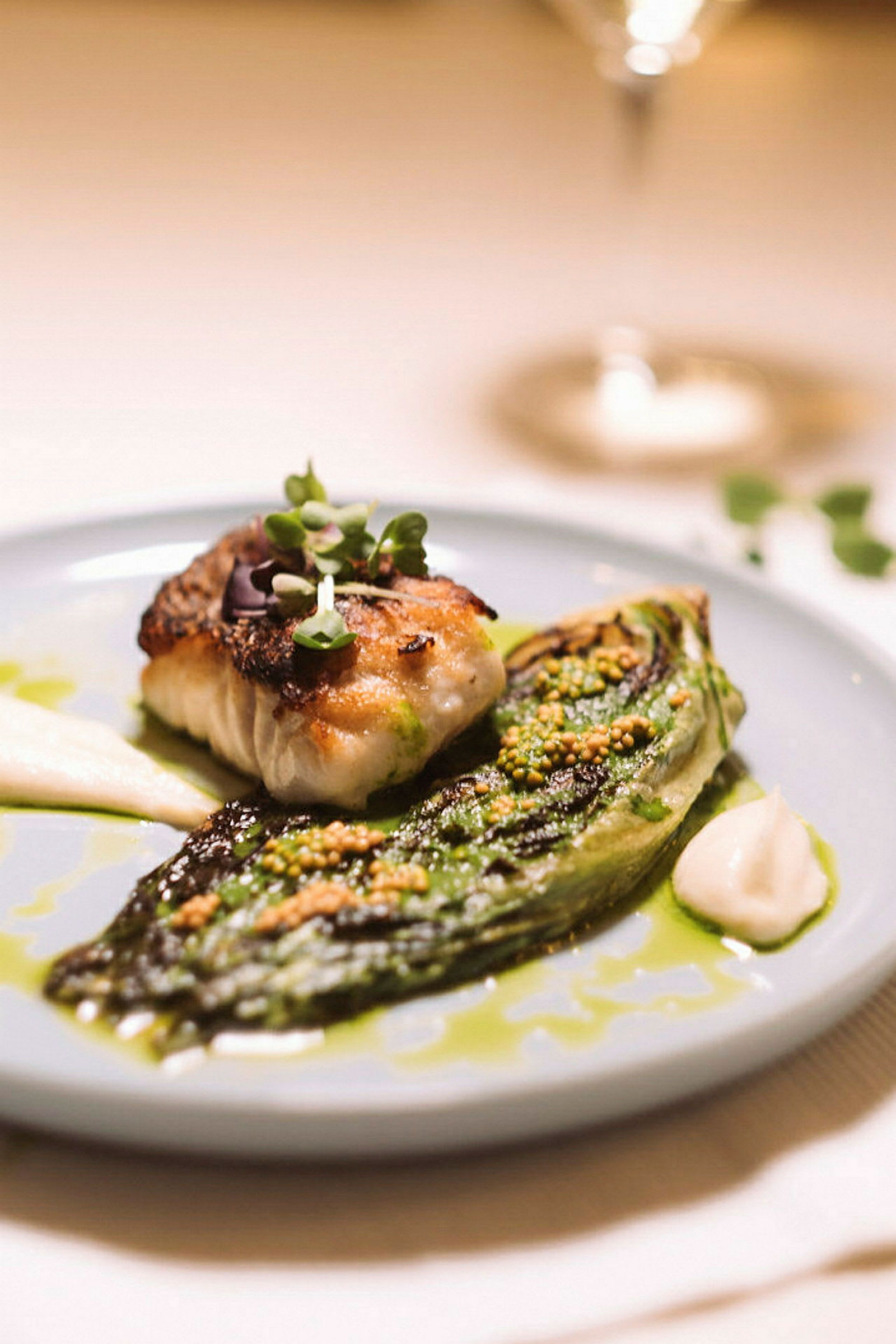 En tallerken med et tilberedt fiskestykke og en grillet salatkile, serveret med sauce og friske urter. (AI-genereret tekst)