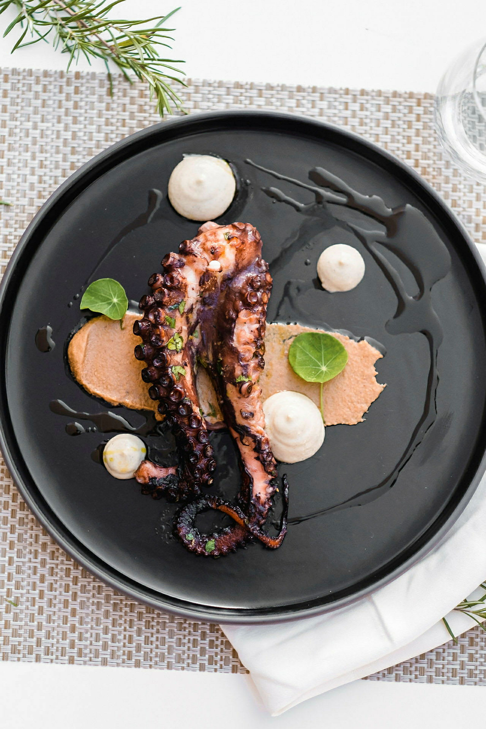 En tallerken med en servering af grillet blæksprutte med sauce og dekorative blade. (AI-genereret tekst)