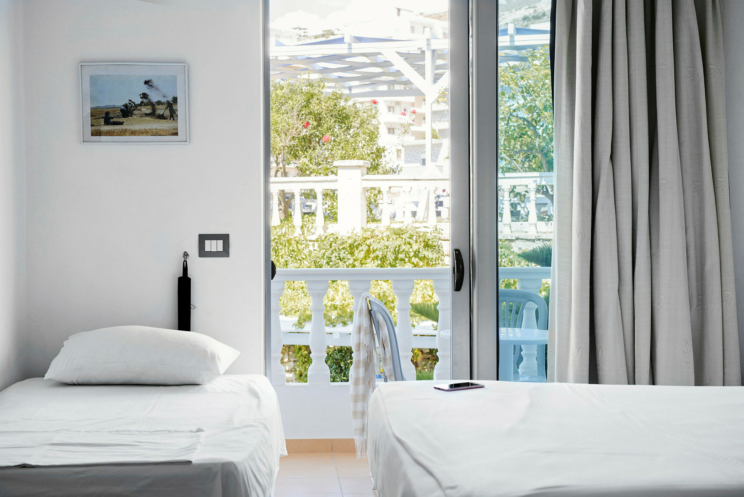 Et lyst hotelværelse med to enkeltsenge, en balkon med udsigt til grønne områder og havemøbler. (AI-genereret tekst)