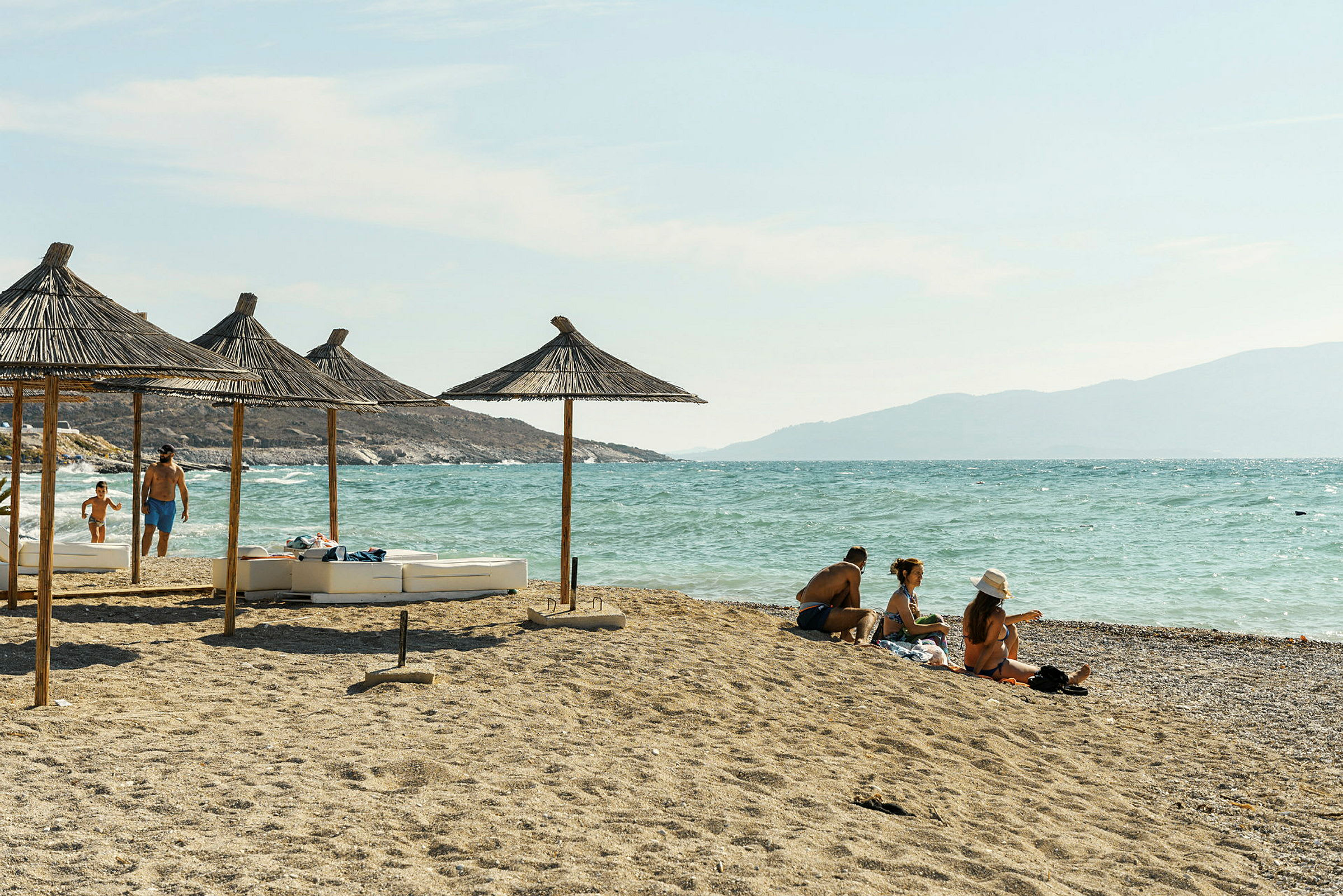 Strand med parasoller af stråtag og mennesker, der nyder solen ved havet. (AI-genereret tekst)