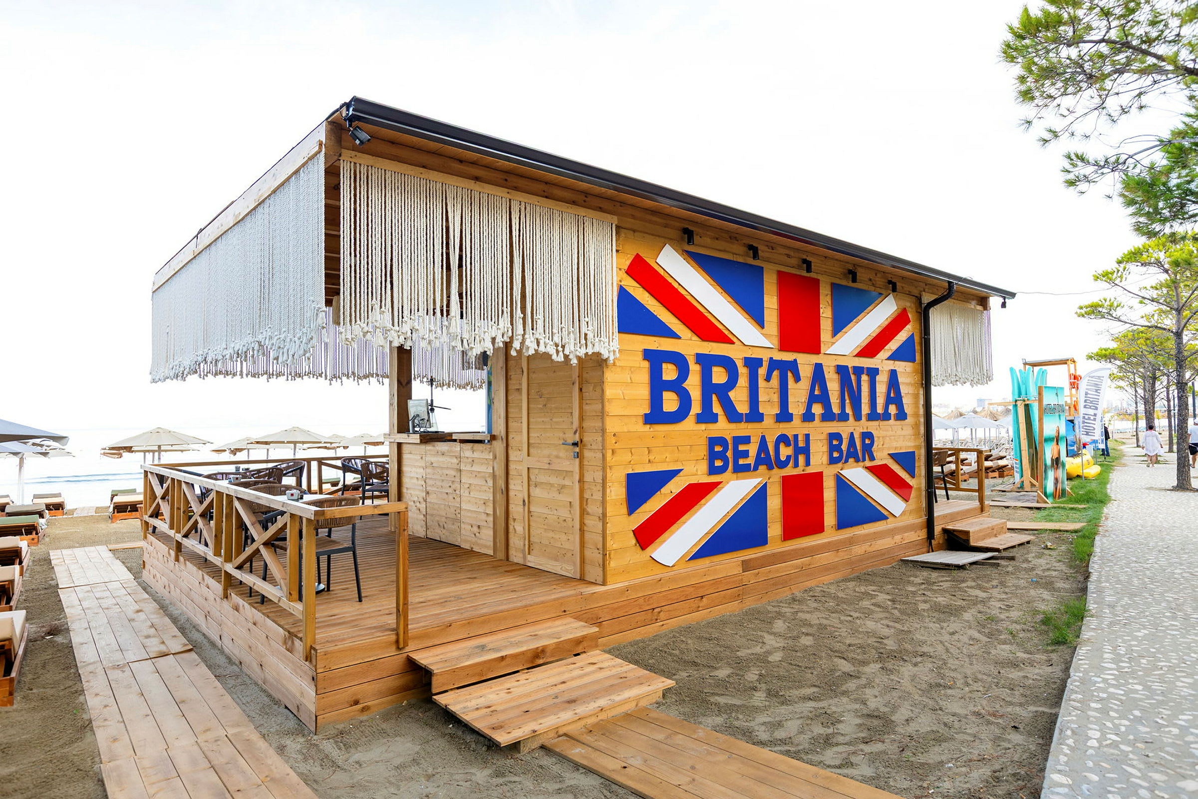 En strandbar med navnet Britania Beach Bar, bygget i træ med dekorationer og siddepladser. (AI-genereret tekst)