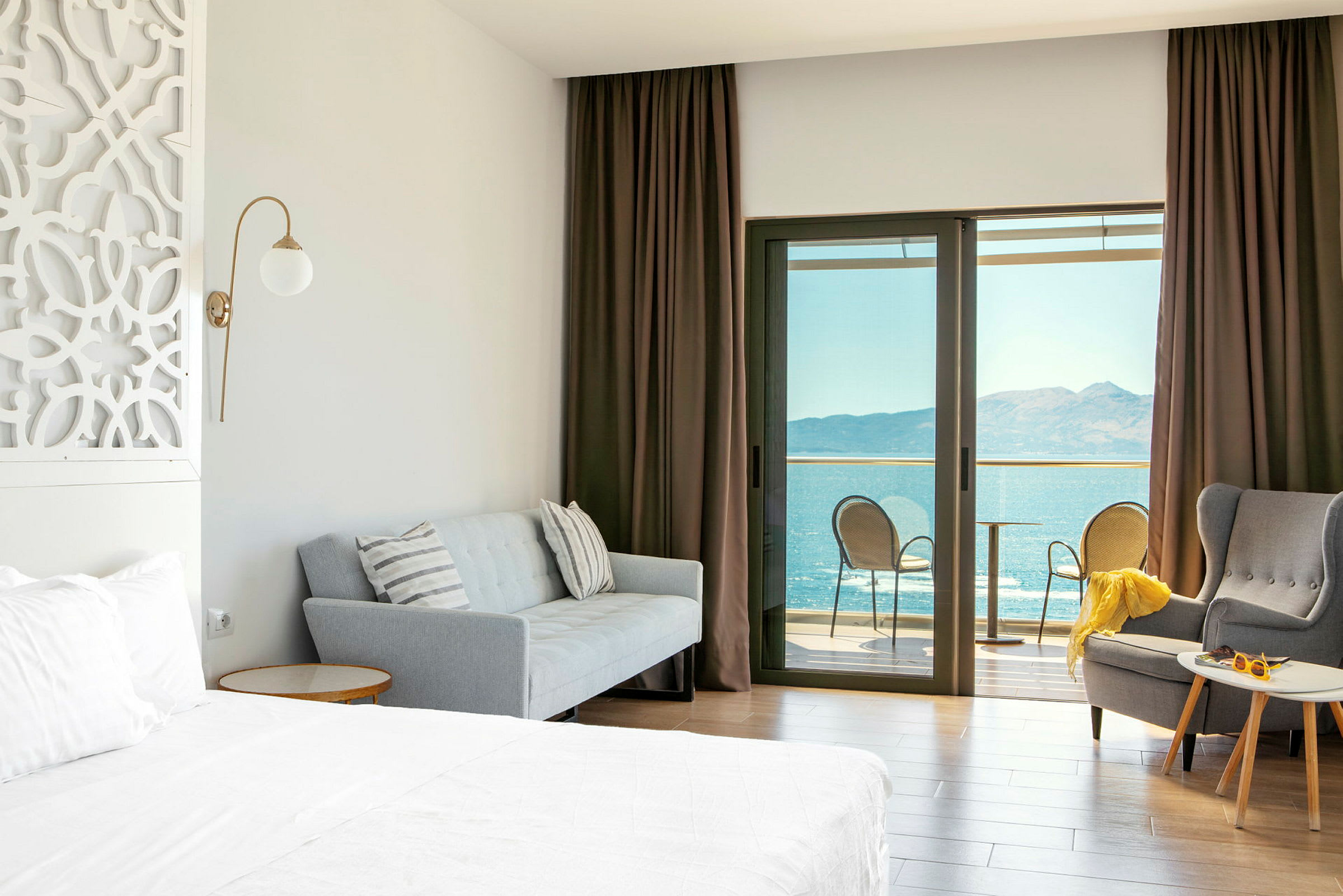 Hotelværelse med seng, sofa, lænestol og altan med havudsigt. (AI-genereret tekst)