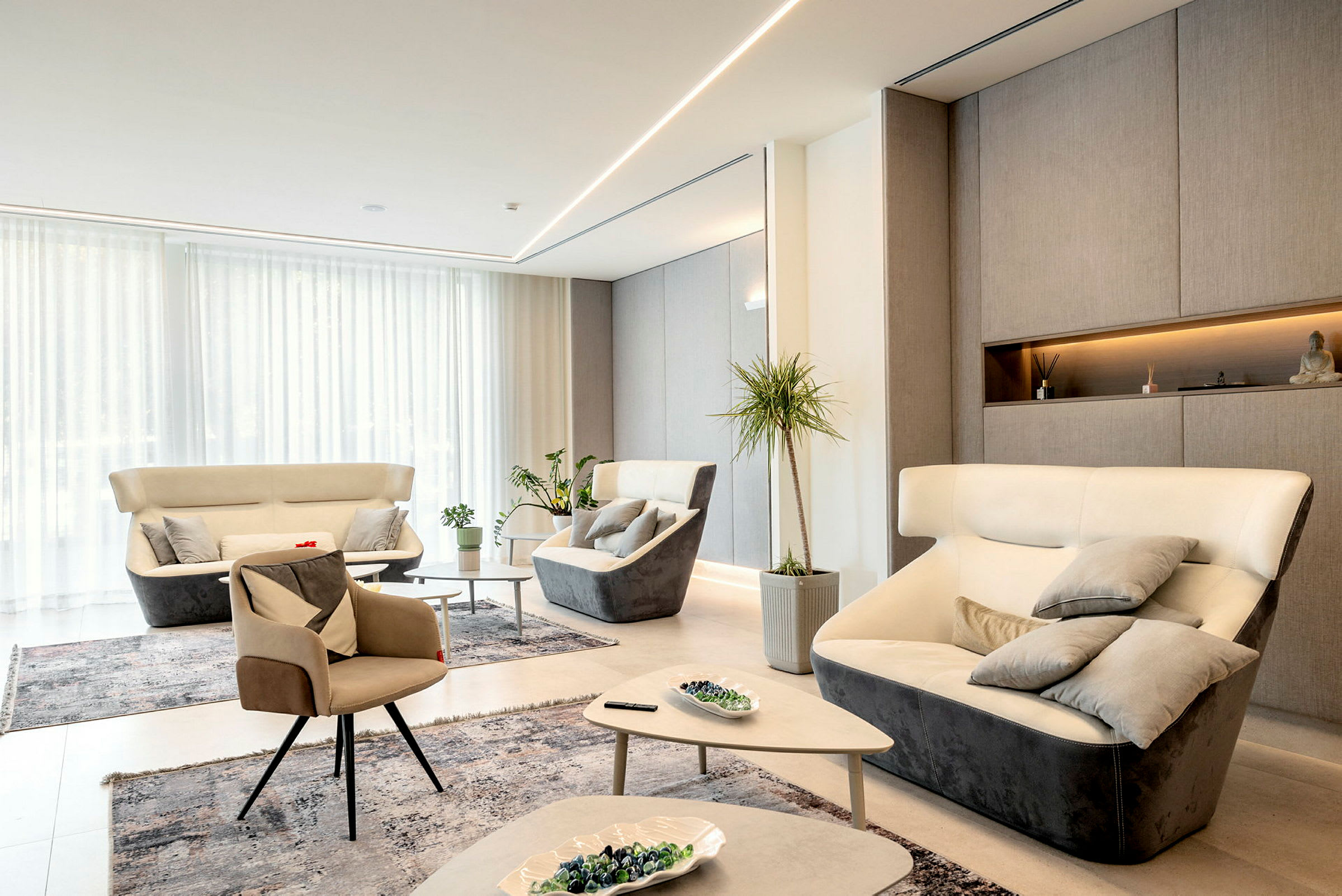 En moderne lounge med lyst interiør, flere komfortable lænestole og sofaer, planter og dekorative genstande. (AI-genereret tekst)
