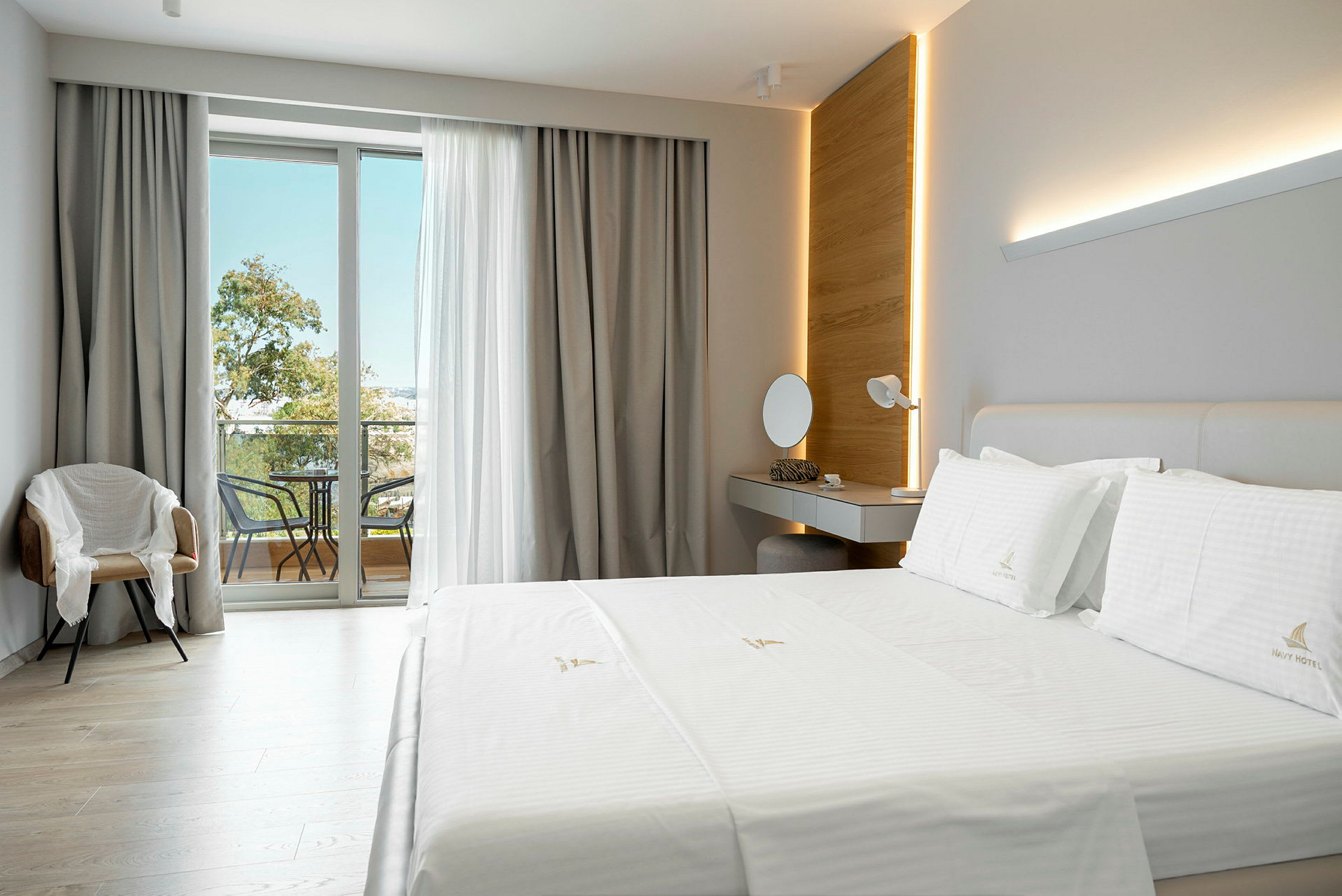 Et moderne hotelværelse med en stor seng, et skrivebord, en stol og en balkon med møbler. (AI-genereret tekst)