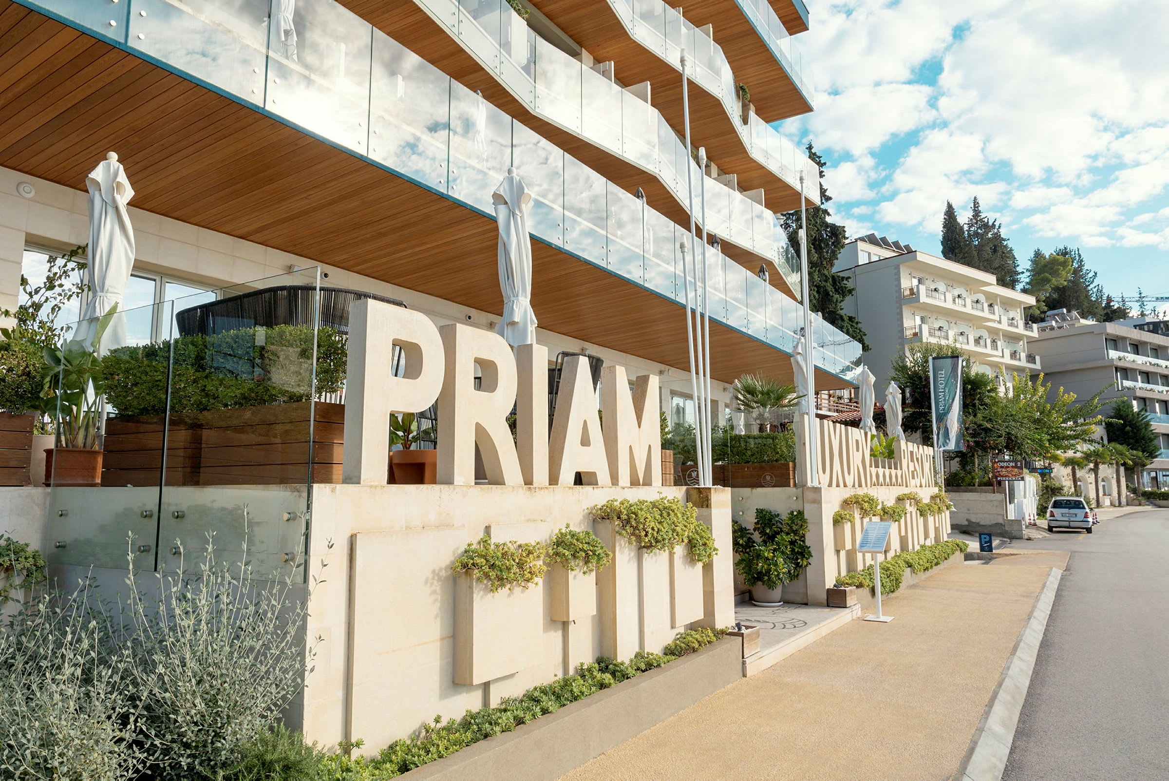 En moderne bygning med skilte der siger 'PRIMAM LUXURY RESORT', omgivet af grønne områder og altaner. (AI-genereret tekst)