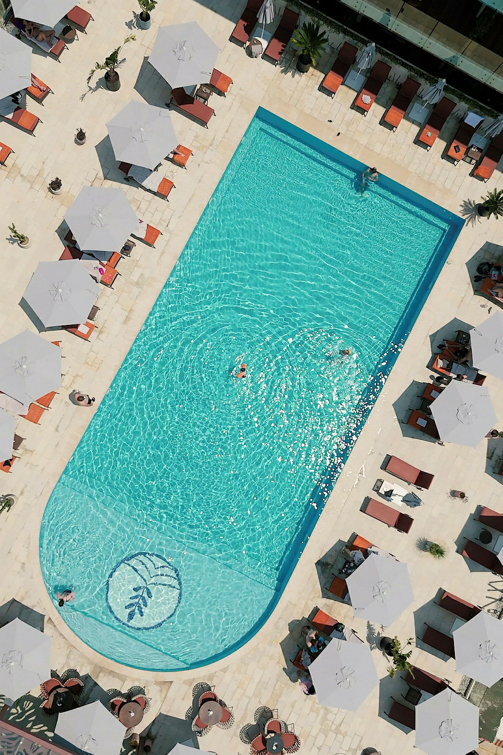 Udsigt ovenfra over en rektangulær pool omgivet af liggestole og parasoller. (AI-genereret tekst)