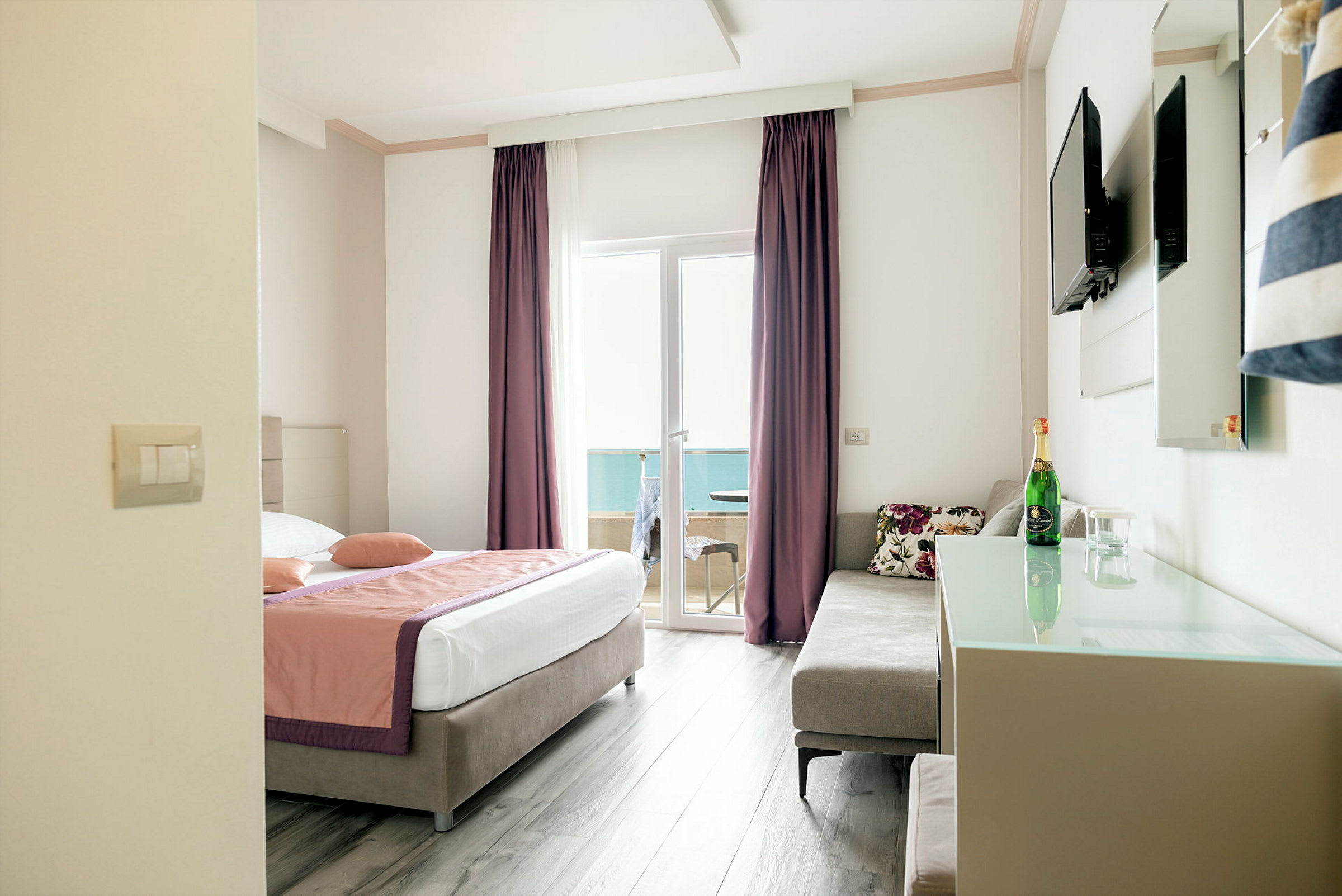Hotelværelse med en dobbeltseng, sofa, tv på væggen og en glasdør, der fører til en balkon. (AI-genereret tekst)