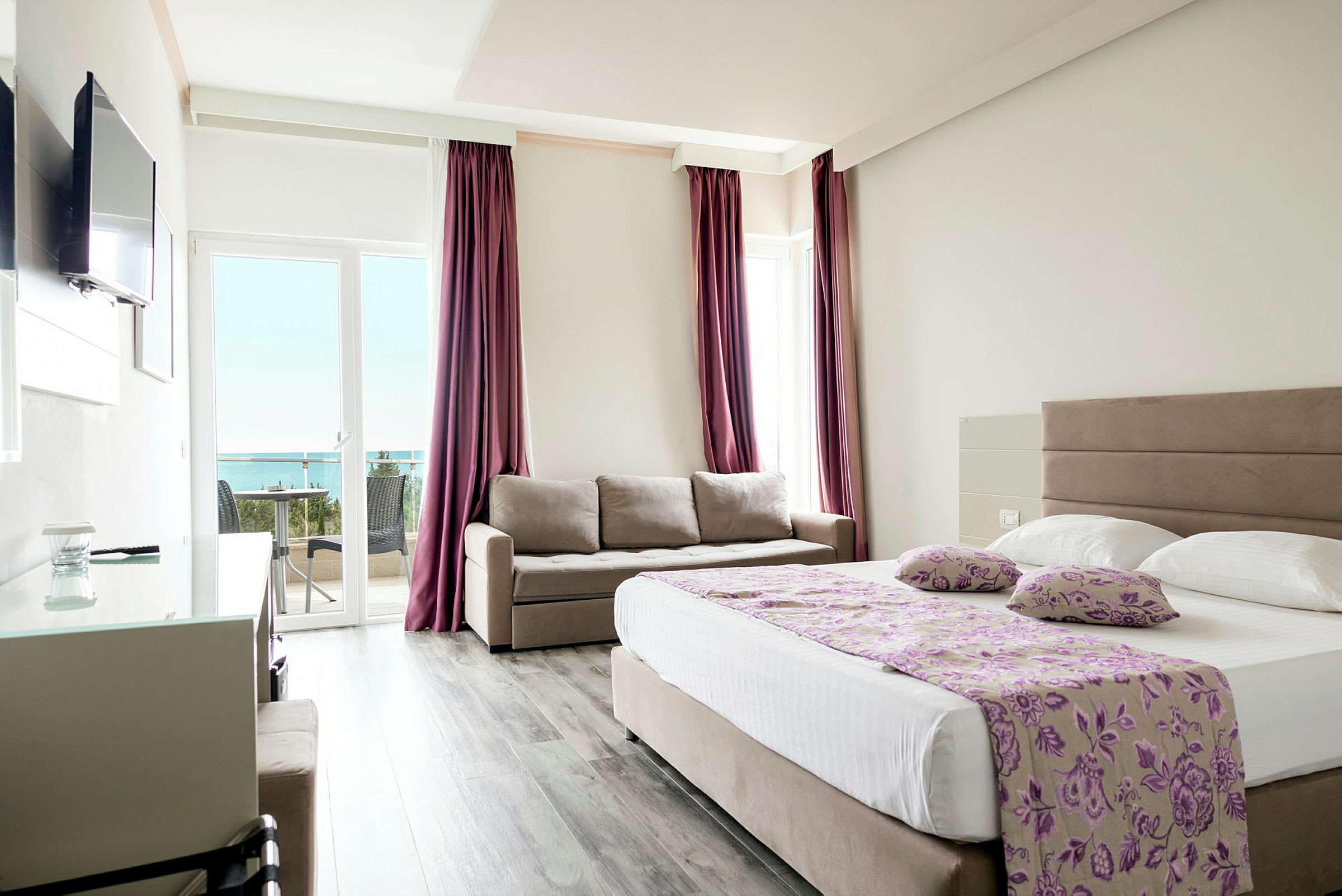 Et hotelværelse med en dobbeltseng, en sofa og en balkon med udsigt over havet. (AI-genereret tekst)