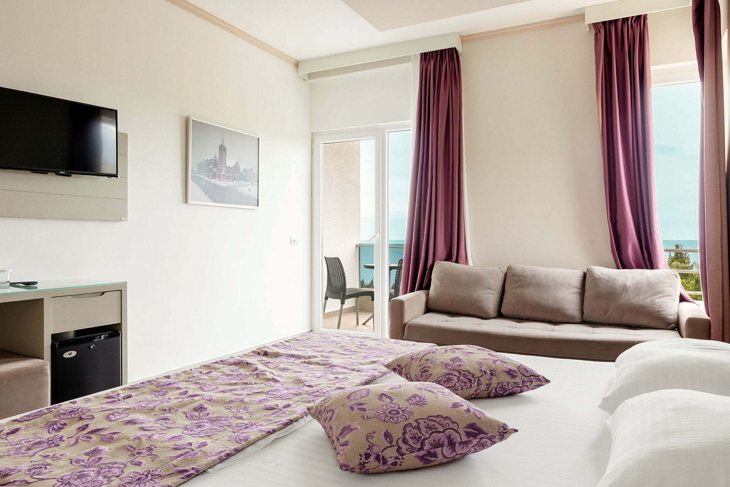 Hotelværelse med seng, sofa, fjernsyn og en balkon med udsigt. (AI-genereret tekst)
