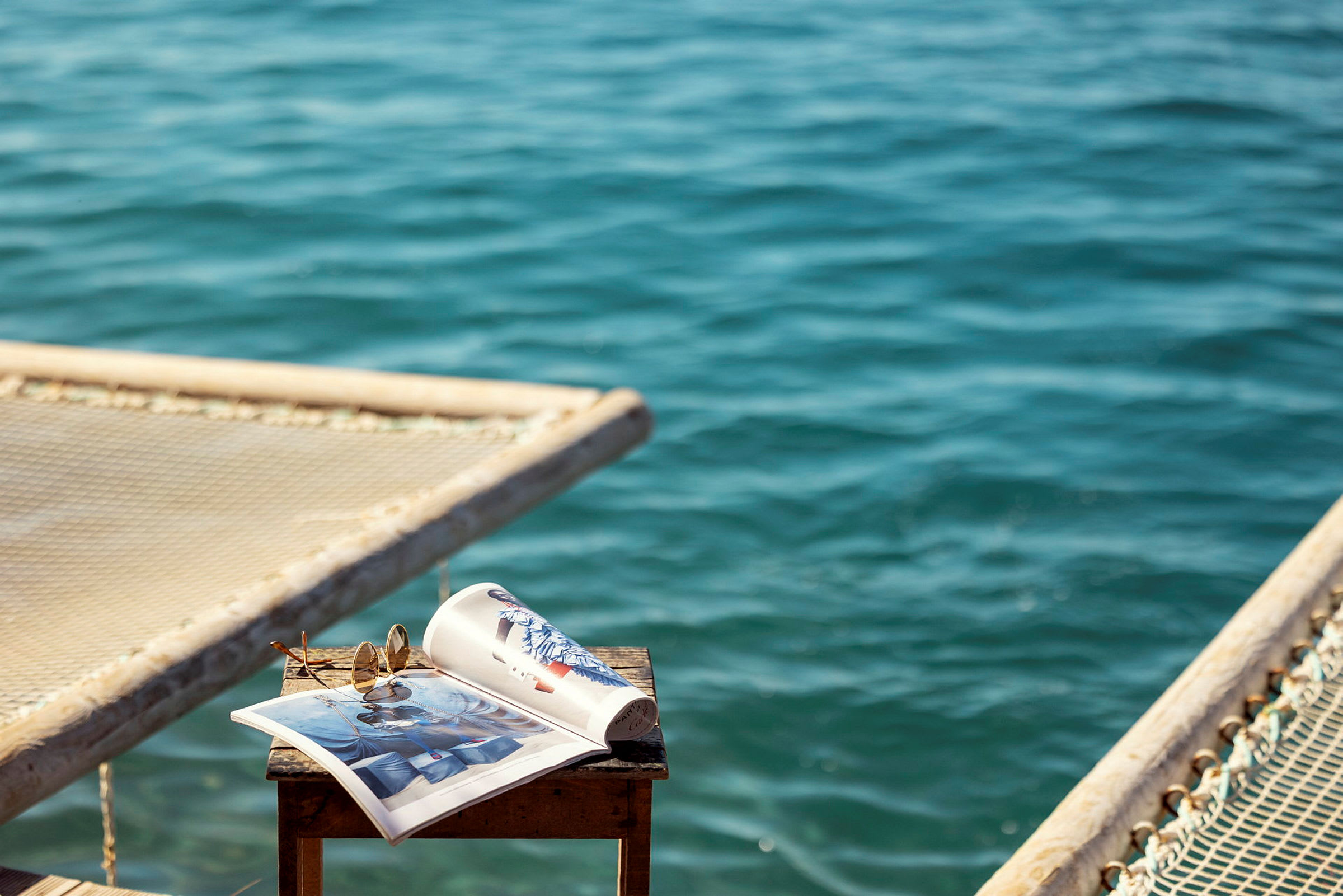 Et bord med et åbent magasin og solbriller, med havet i baggrunden. (AI-genereret tekst)