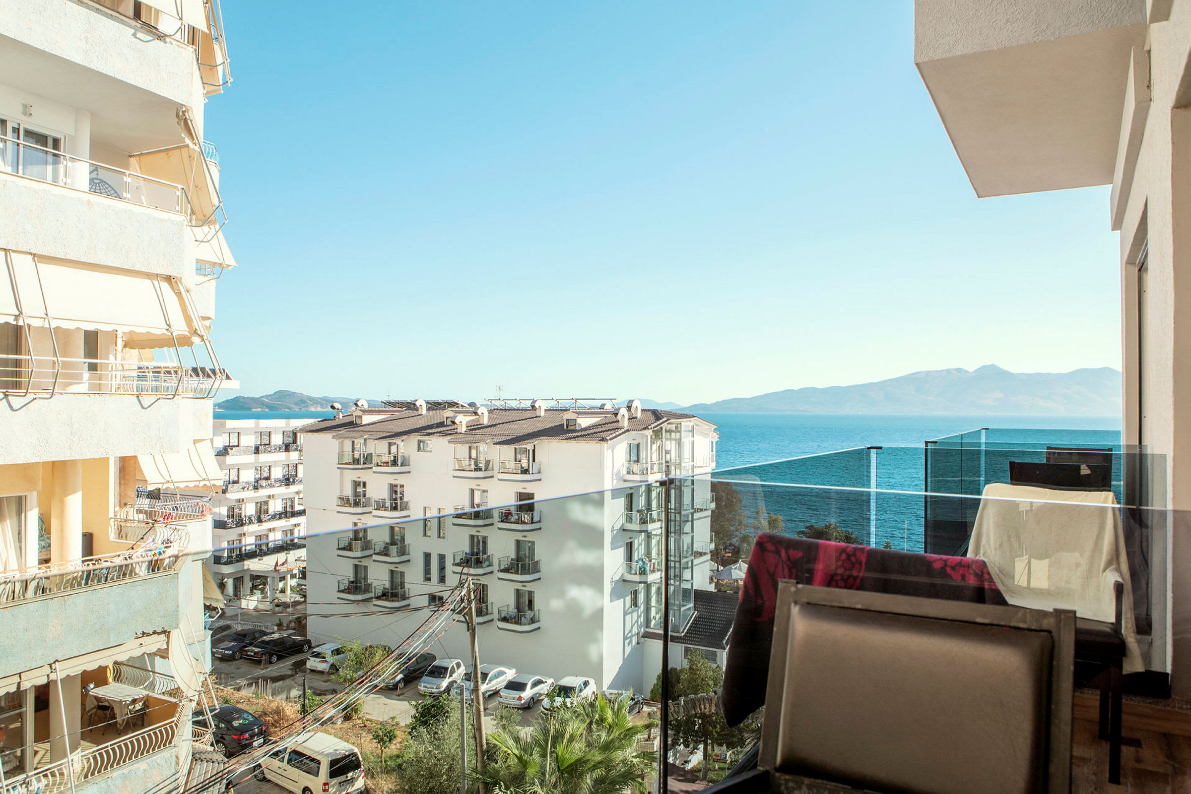 Udsigt fra en balkon over bygninger og havet med bjerge i det fjerne. (AI-genereret tekst)