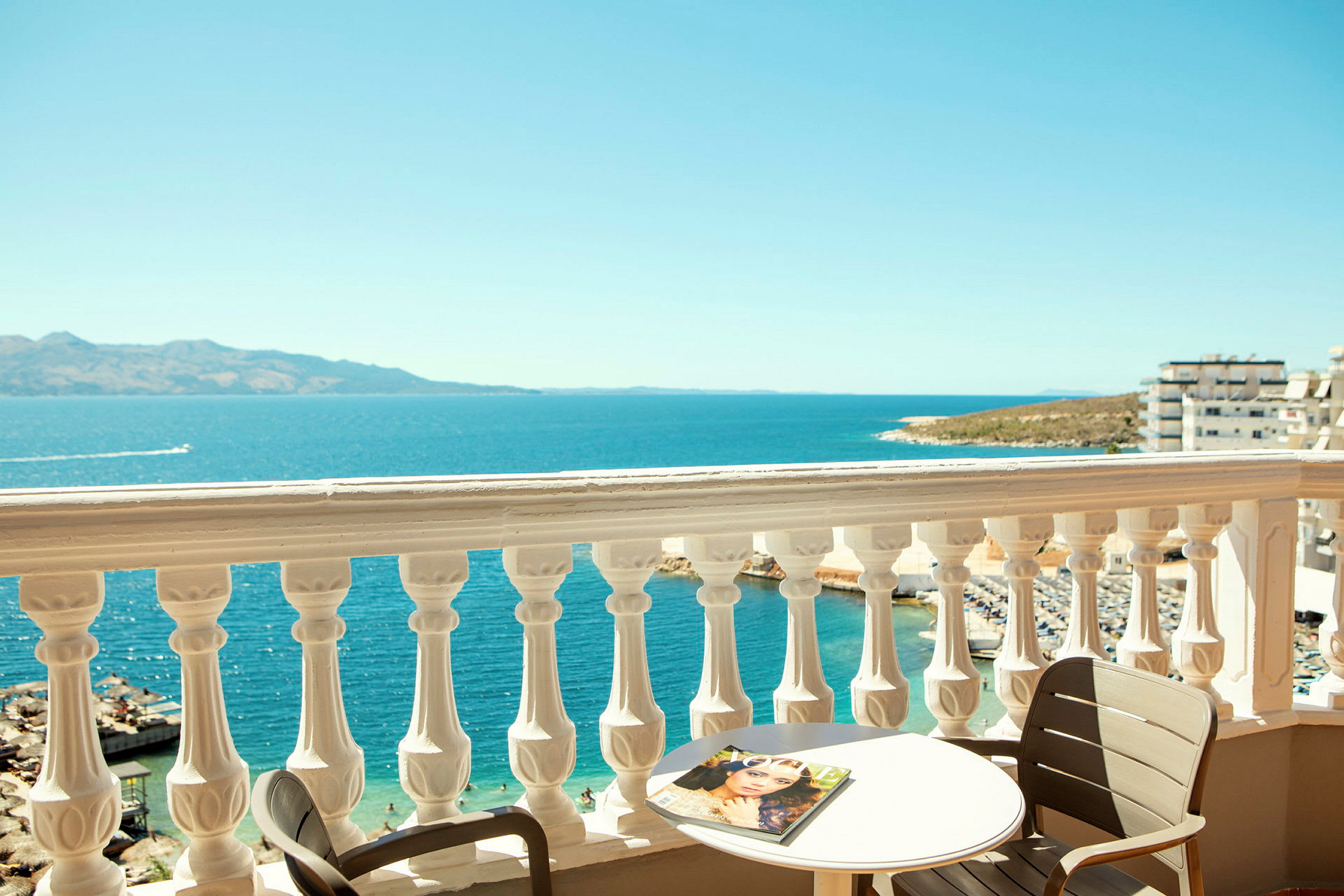 Udsigt fra en balkon med et hvidt rækværk over havet, et bord og en stol. (AI-genereret tekst)