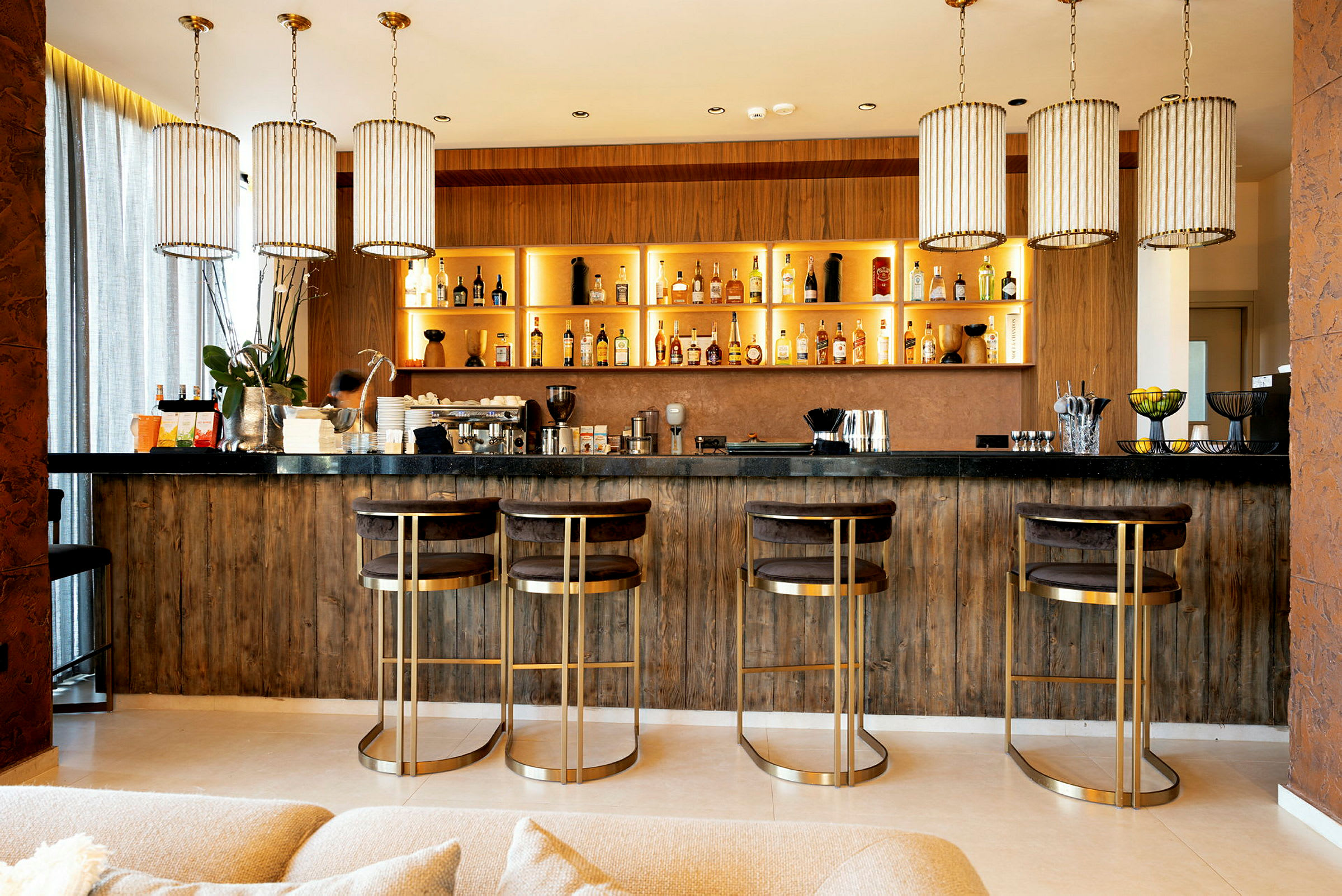 En elegant bar med fire høje stole og hylder fyldt med flasker. (AI-genereret tekst)