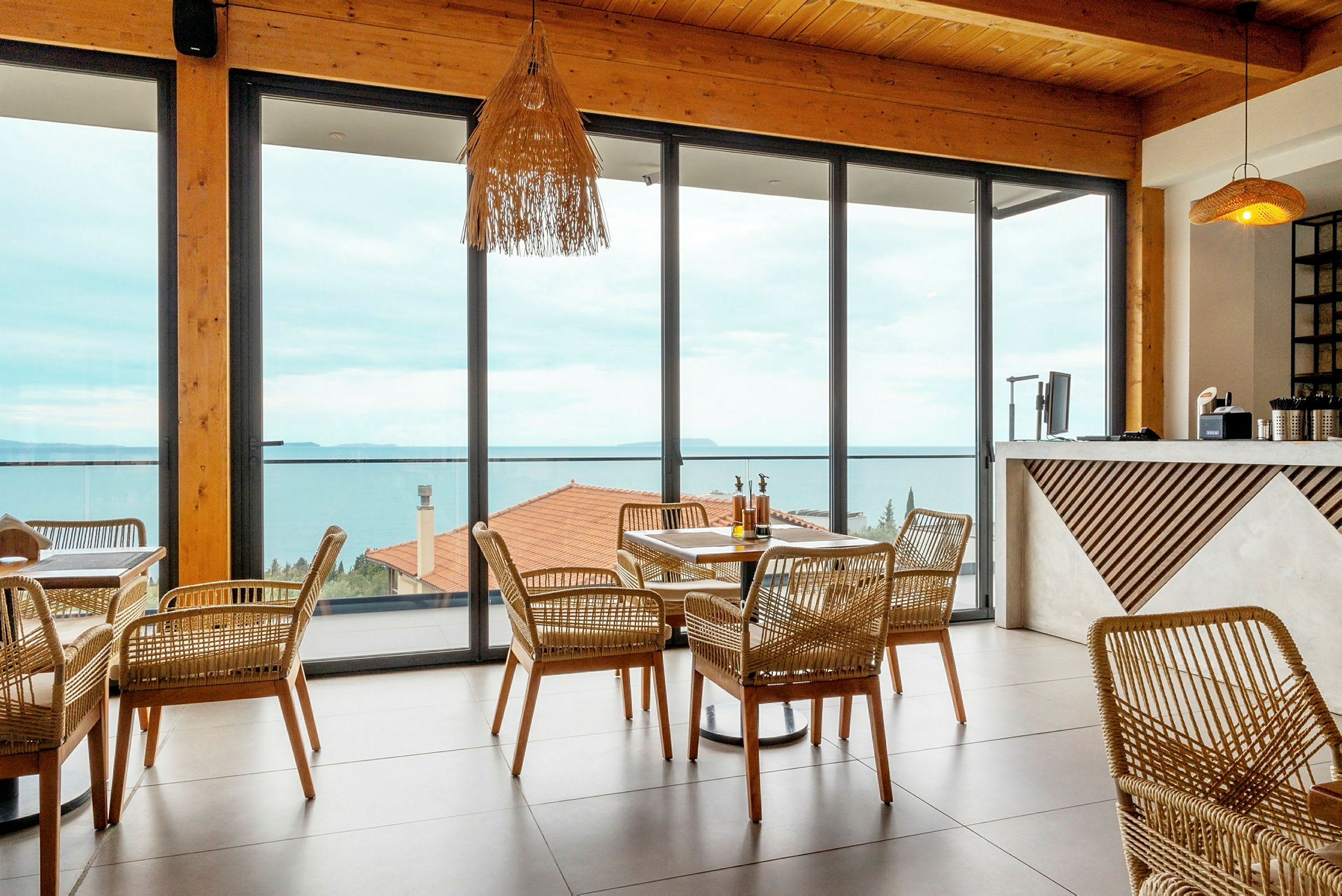 En restaurant med rottemøbler og store vinduer mod havet. (AI-genereret tekst)