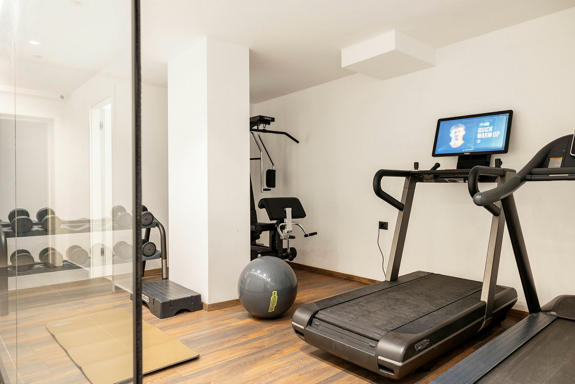 Et fitnessrum med løbebånd, træningsbænk og håndvægte. (AI-genereret tekst)