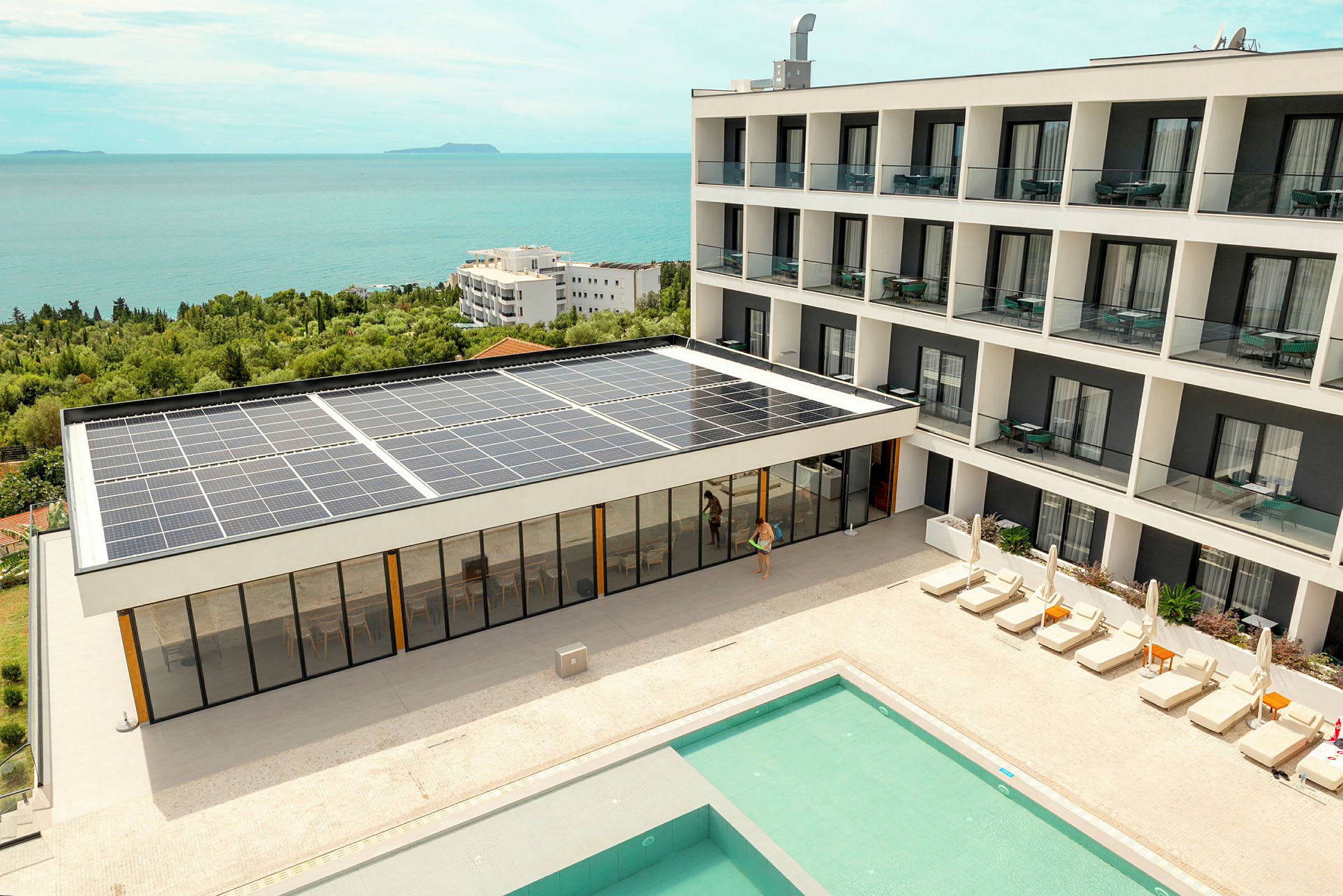 Hotelbygning med solpaneler, pool og liggestole, tæt på kysten. (AI-genereret tekst)