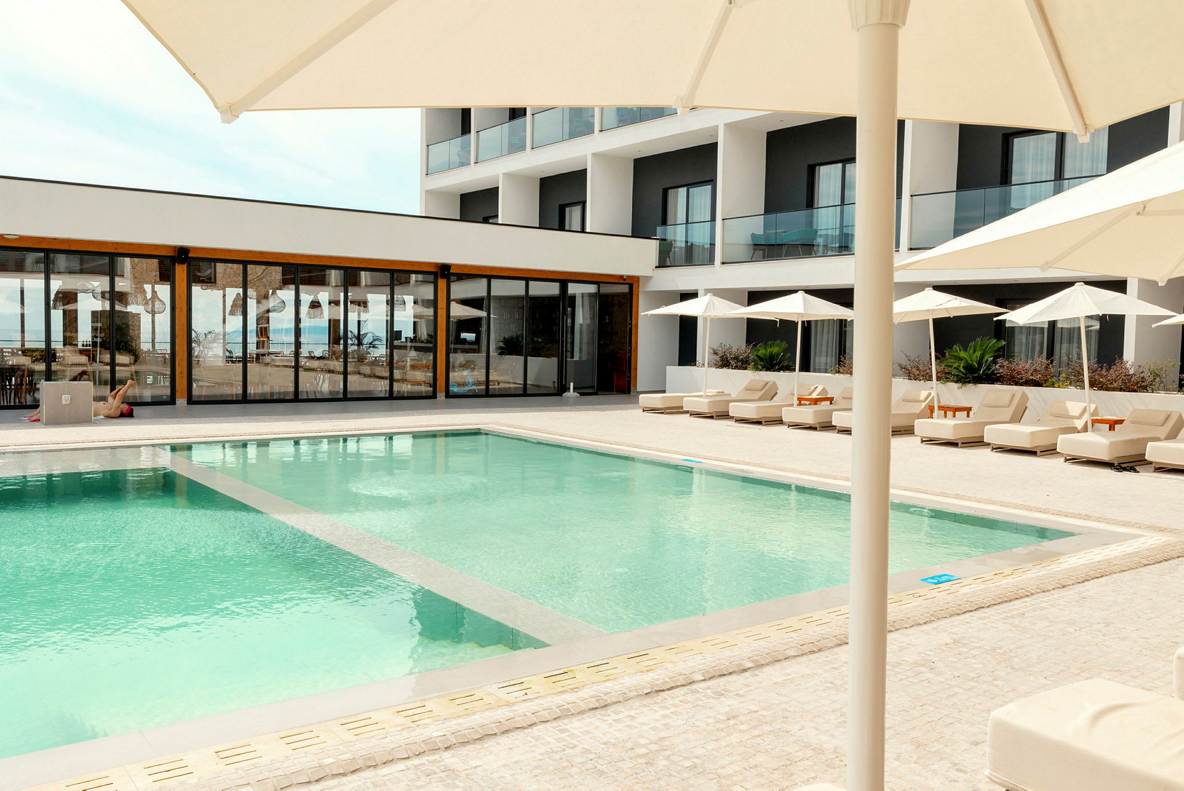 Udendørs swimmingpool ved et moderne hotel med solsenge og parasoller. (AI-genereret tekst)